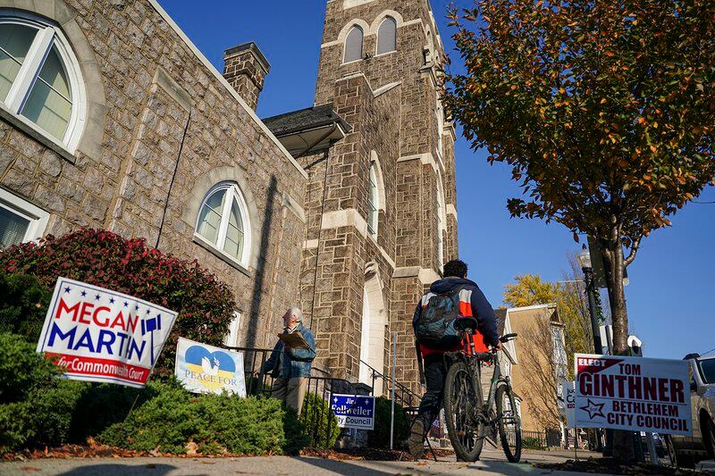 A person walking with a bike crosses in front of a large church with campaign signs on the grass out front.