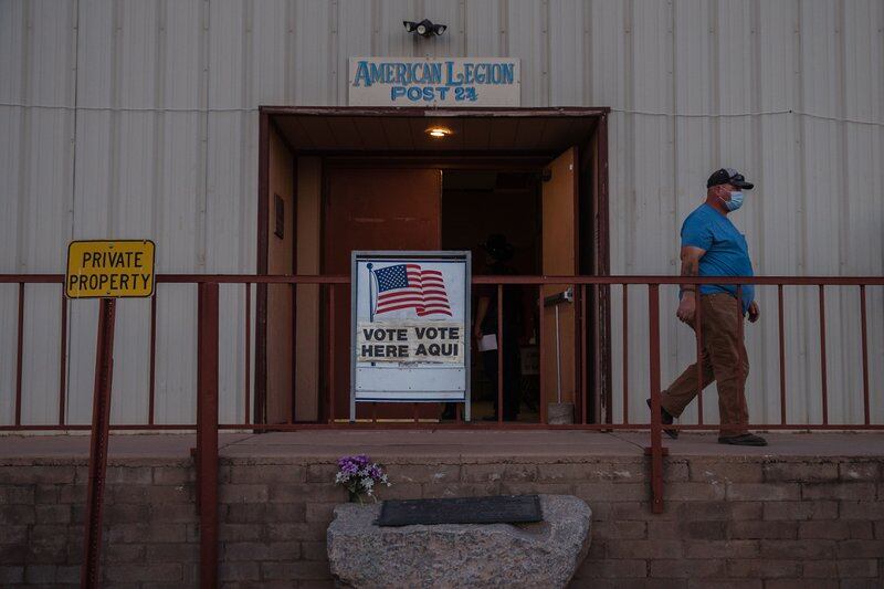 A man walks alongside a white building with a “Vote Here / Vote Aqui” sign out front of its open double doors.