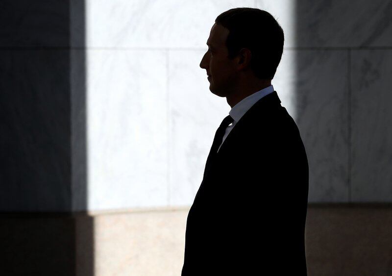 A profile view of Mark Zuckerberg wearing a suit in a dimly lit hallway.