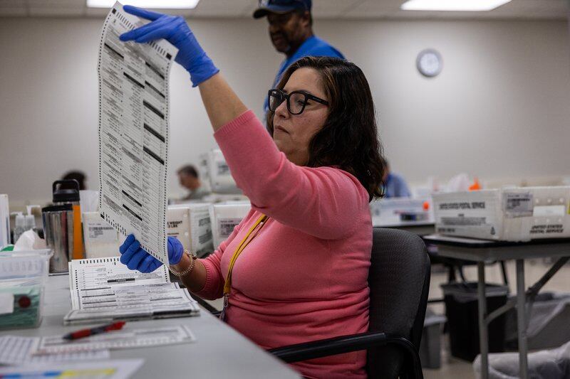 woman in pink shirt with blue gloves on holds up long ballot