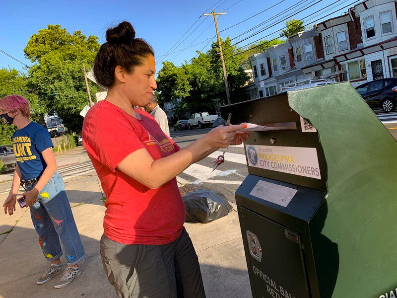 A voter drops a ballot in a green drop box in on the street in Philadelphia.
