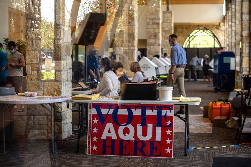 A sign reading “vote here aqui” hangs from a table in front of a row of polling stations and poll workers