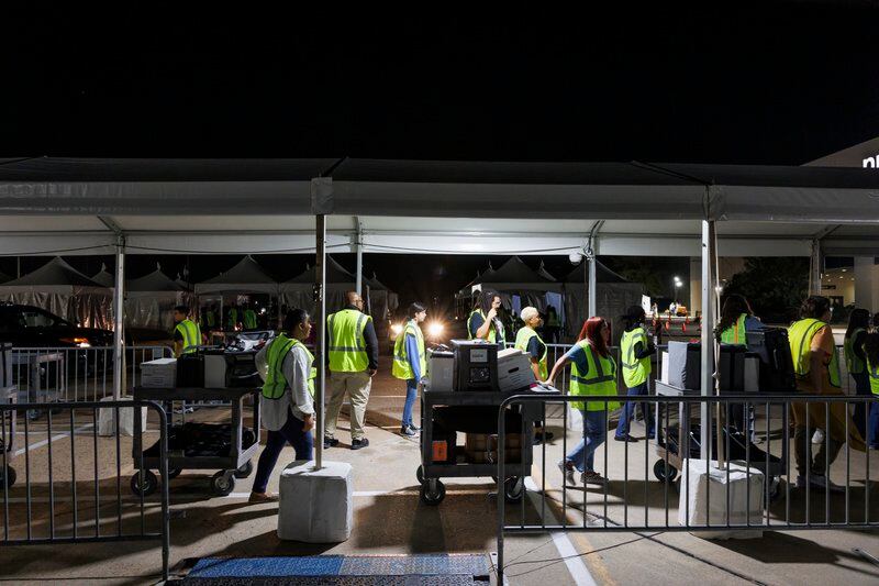 A line of people wearing bright safety vests pull equipment from a parking lot and into a building