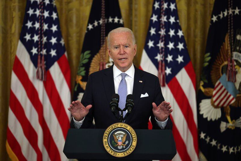 Joe Biden standing at a lectern bearing the presidential seal, before a background of U.S. flags
