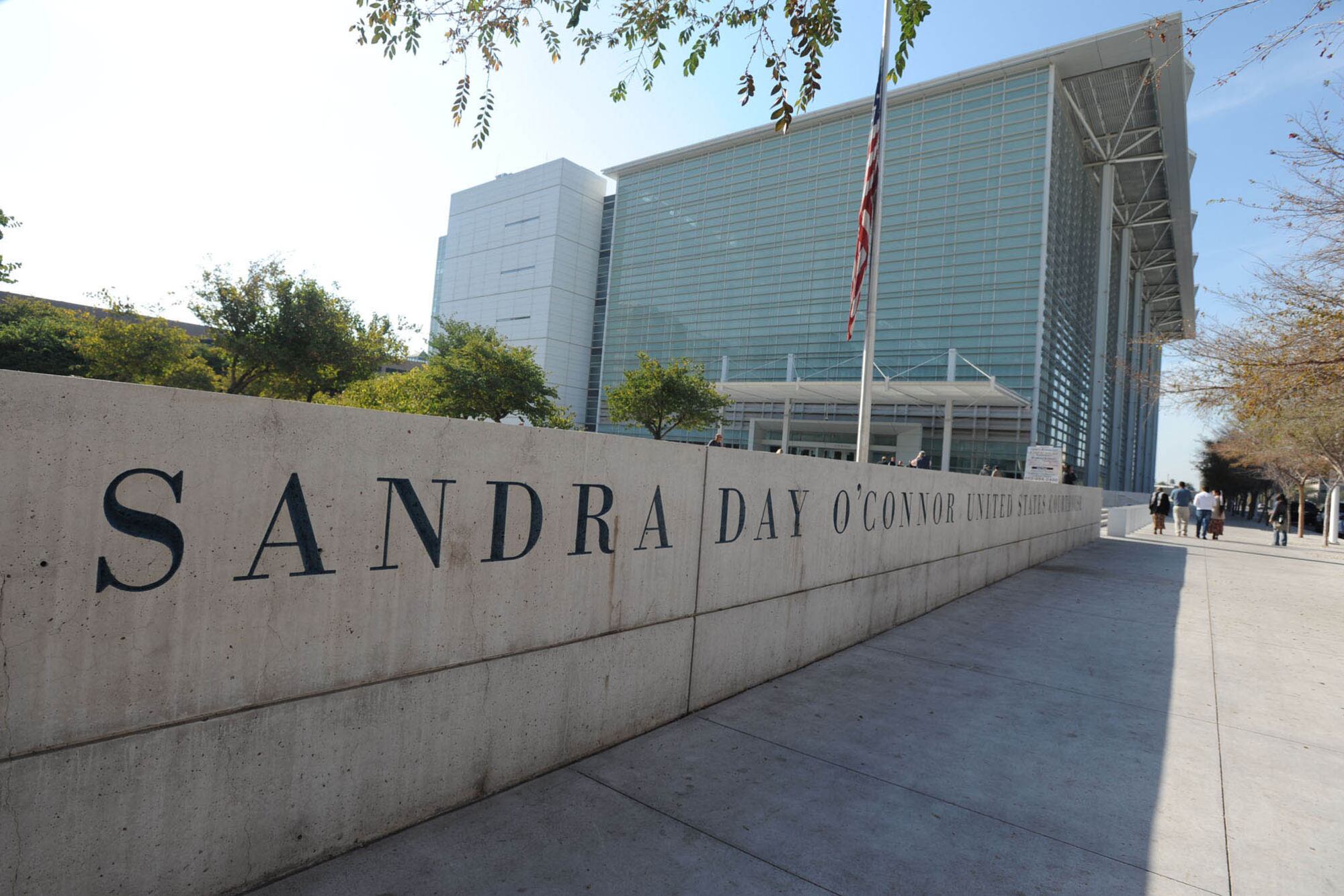 A photo of a low concrete wall leading up the the front of a tall glass building. The wall is etched with the words "Sandra Day O'Connor"