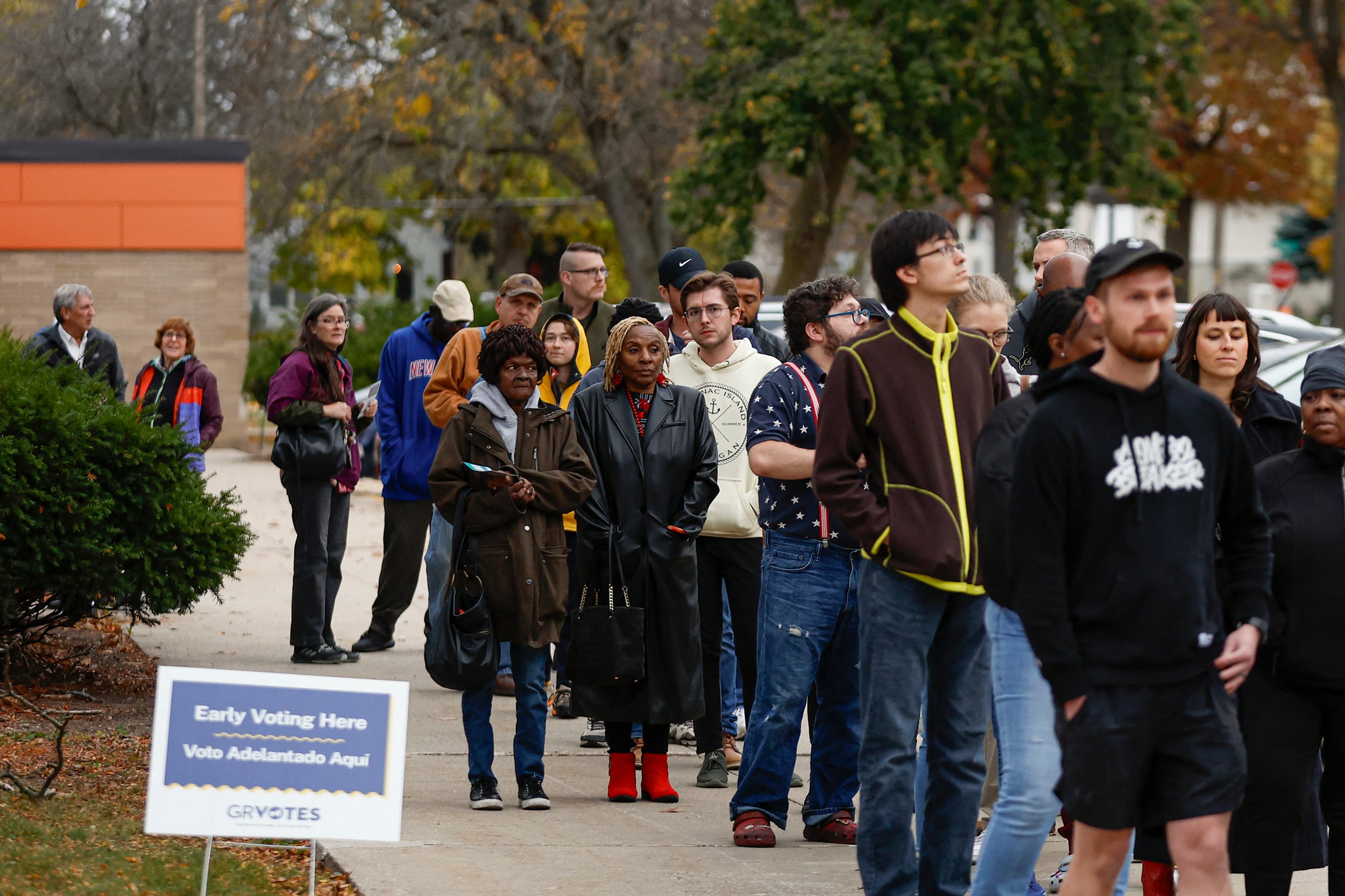 A photograph of a large group of people stand in line outside on a chilly day to vote.
