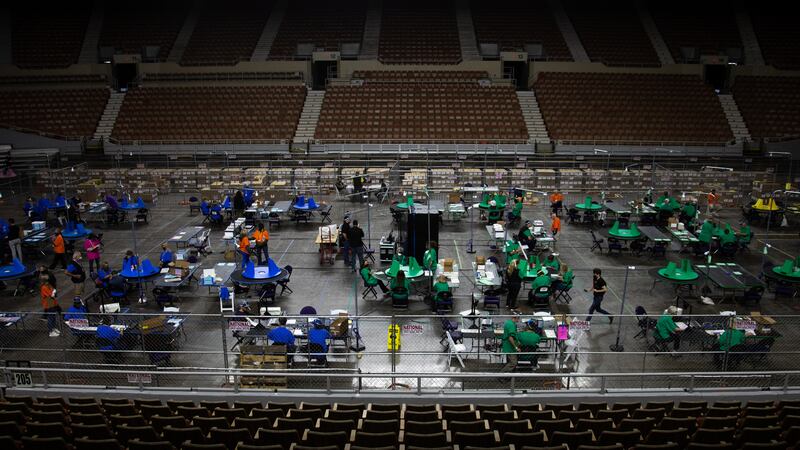 People in colored T-shirts work at several tables on the main floor of a sports arena