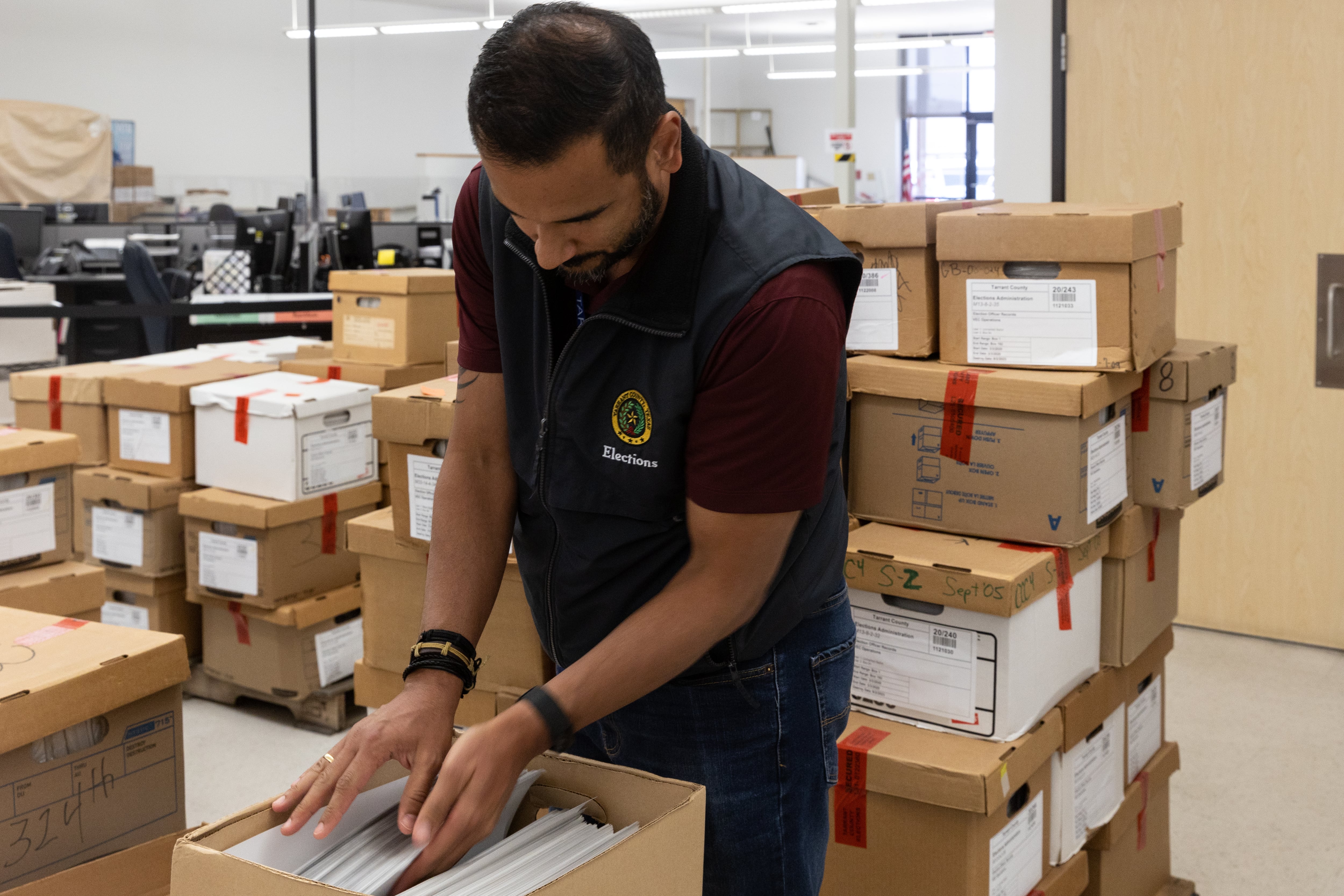 A man reaches into a box of ballots in a room filled with boxes.