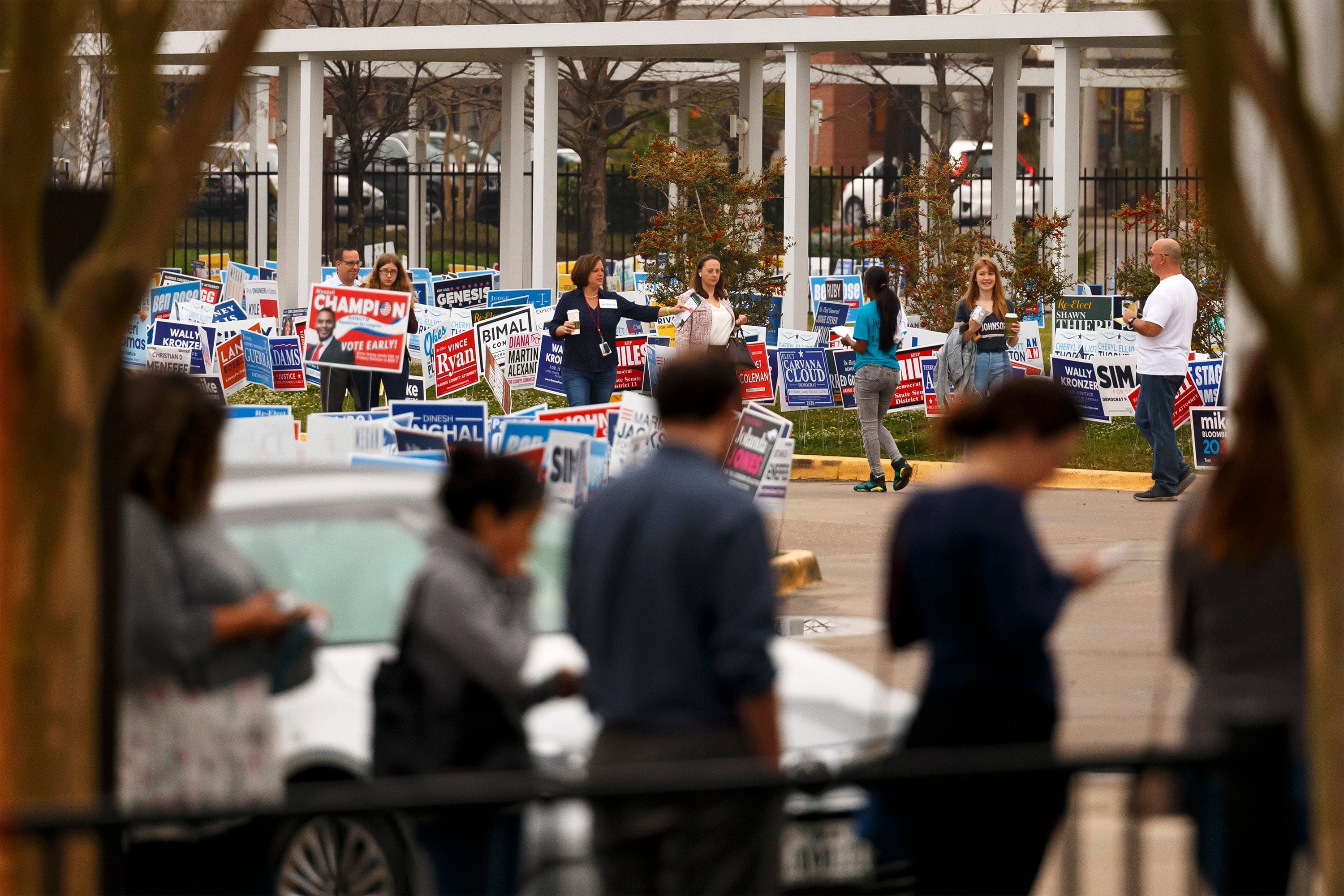 People stand on a sidewalk near political candidates’ campaign signs