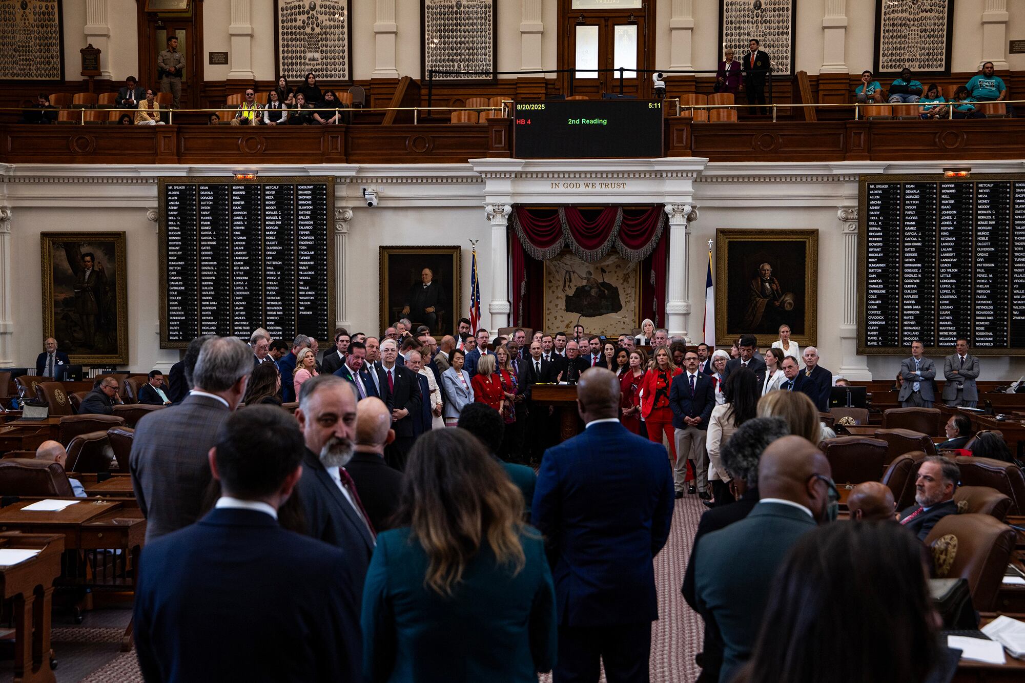 A photograph of a large group of adults in suits standing in a large Texas State Capitol meeting room.