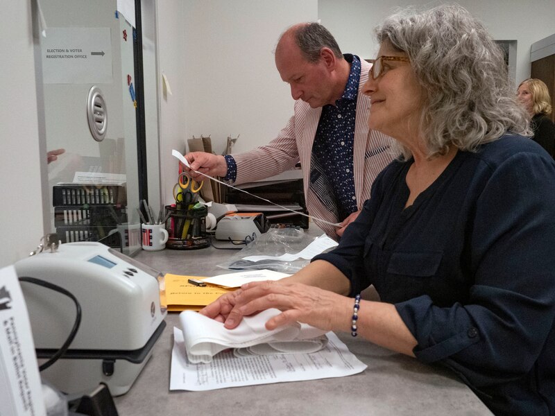 Two people stand and work from a desk with papers and various things.