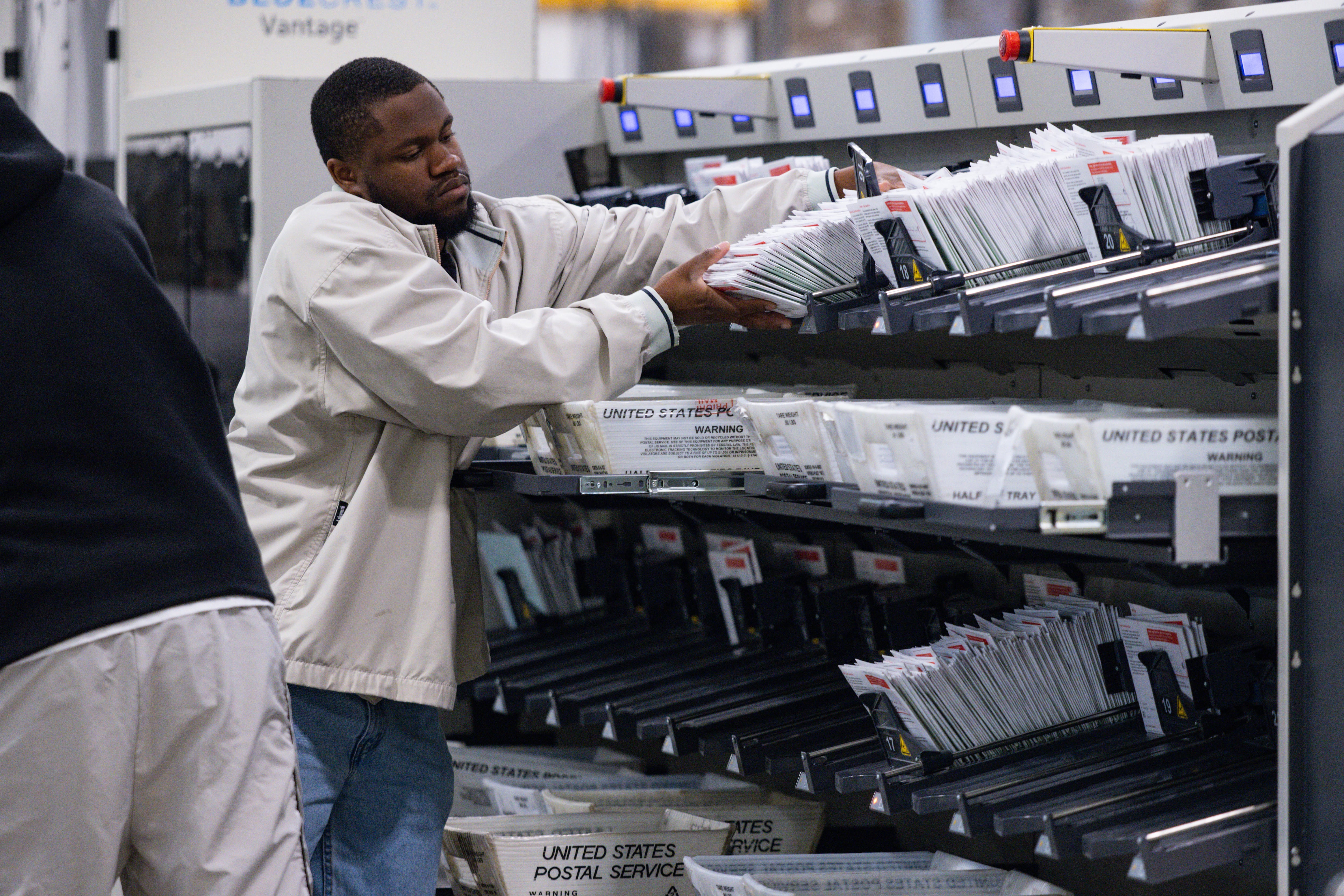 A man in a white jackets handles a bunch of white envelopes.