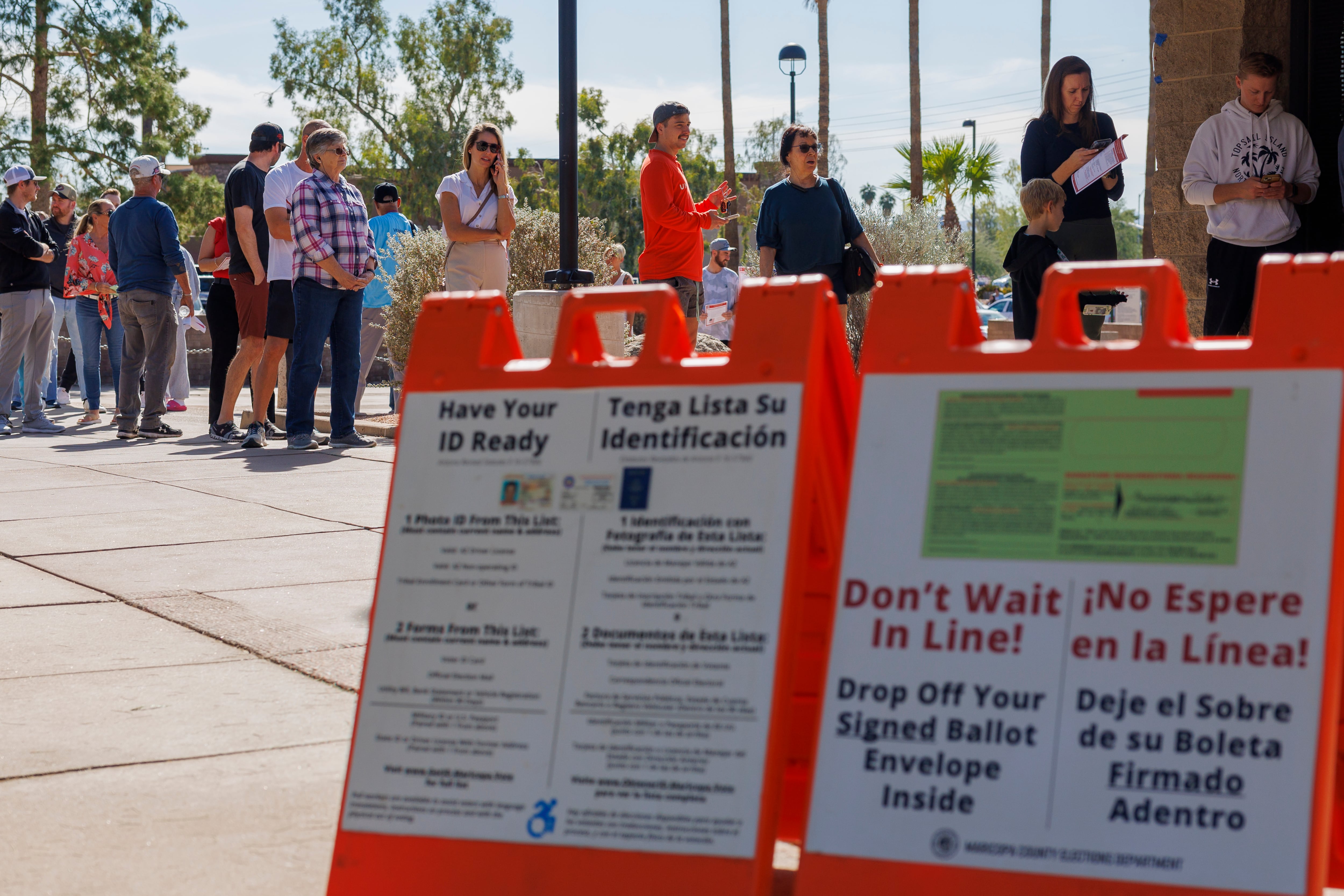 A line of people stand behind two red signs.