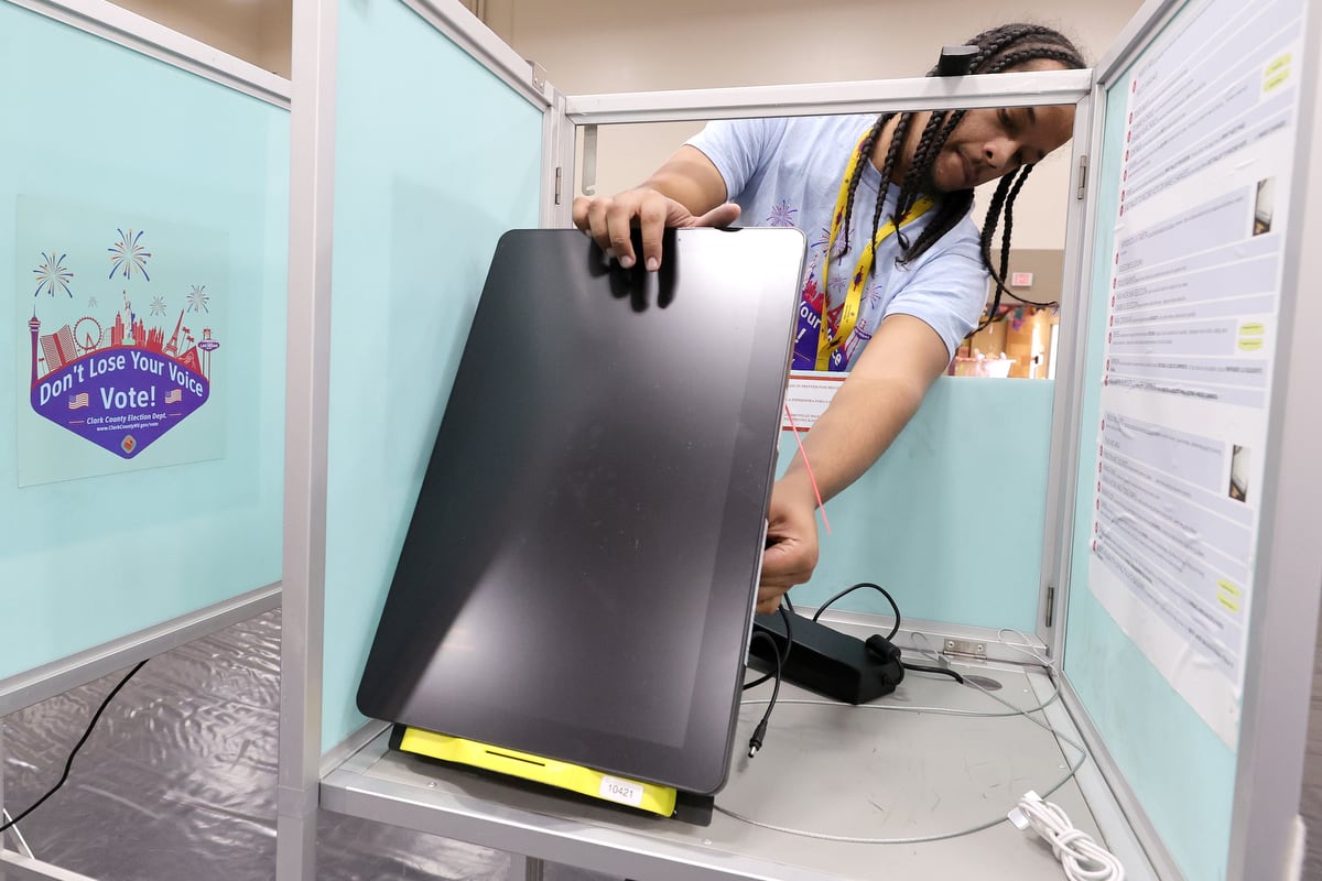 A man holds a rectangular machine vertically in front of him and plugs in a cord.
