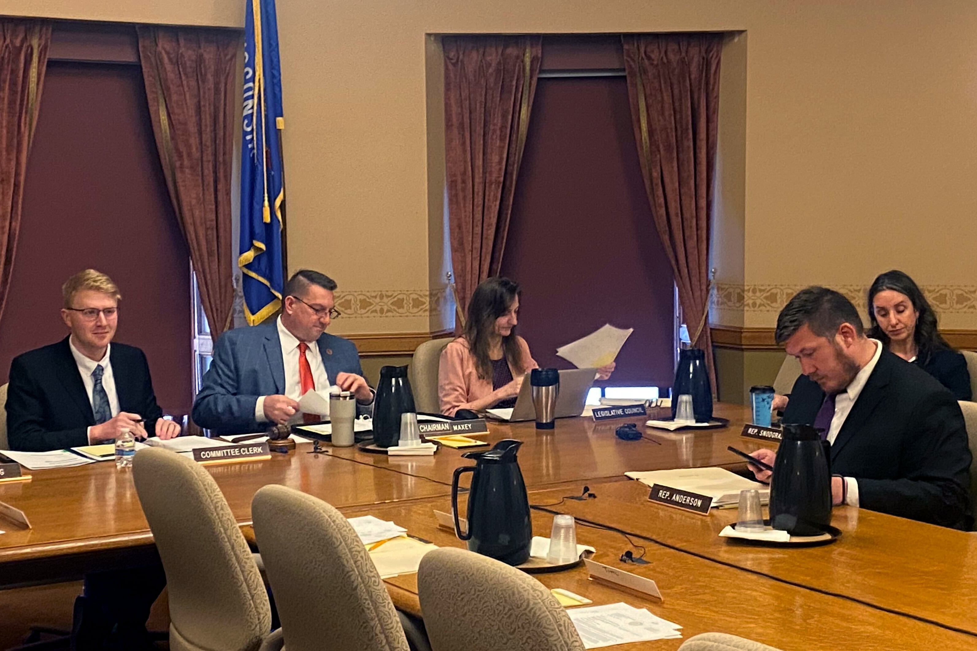 Five people in business attire sit around a large wooden table in a conference room.