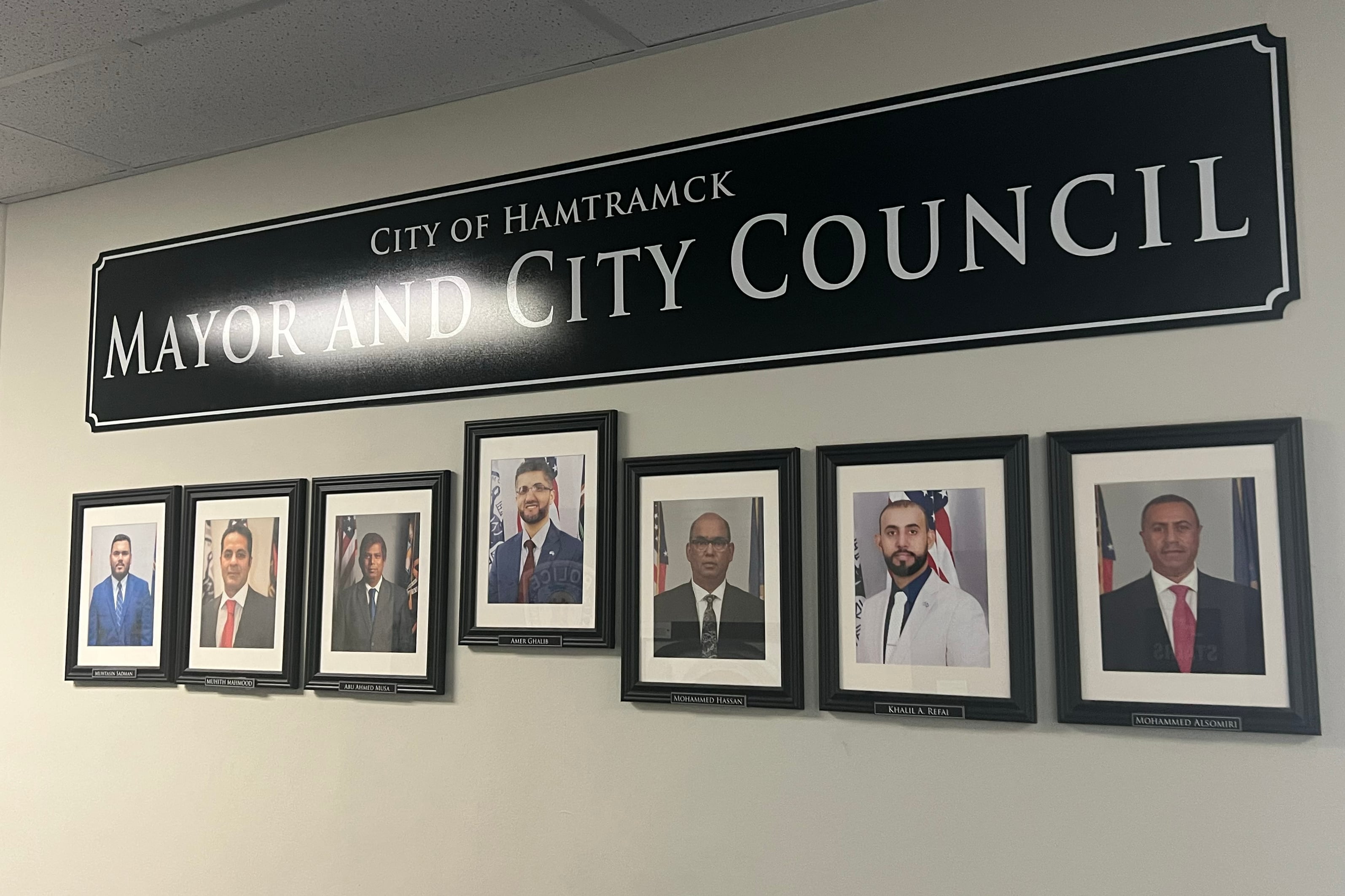 A photograph of a wall of portraits with a sign that reads "City of Hamtramck Mayor and City Council."
