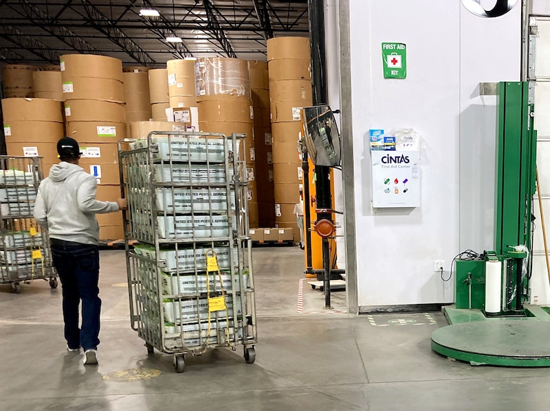 A person rolls a cart full of ballot boxes in a warehouse.