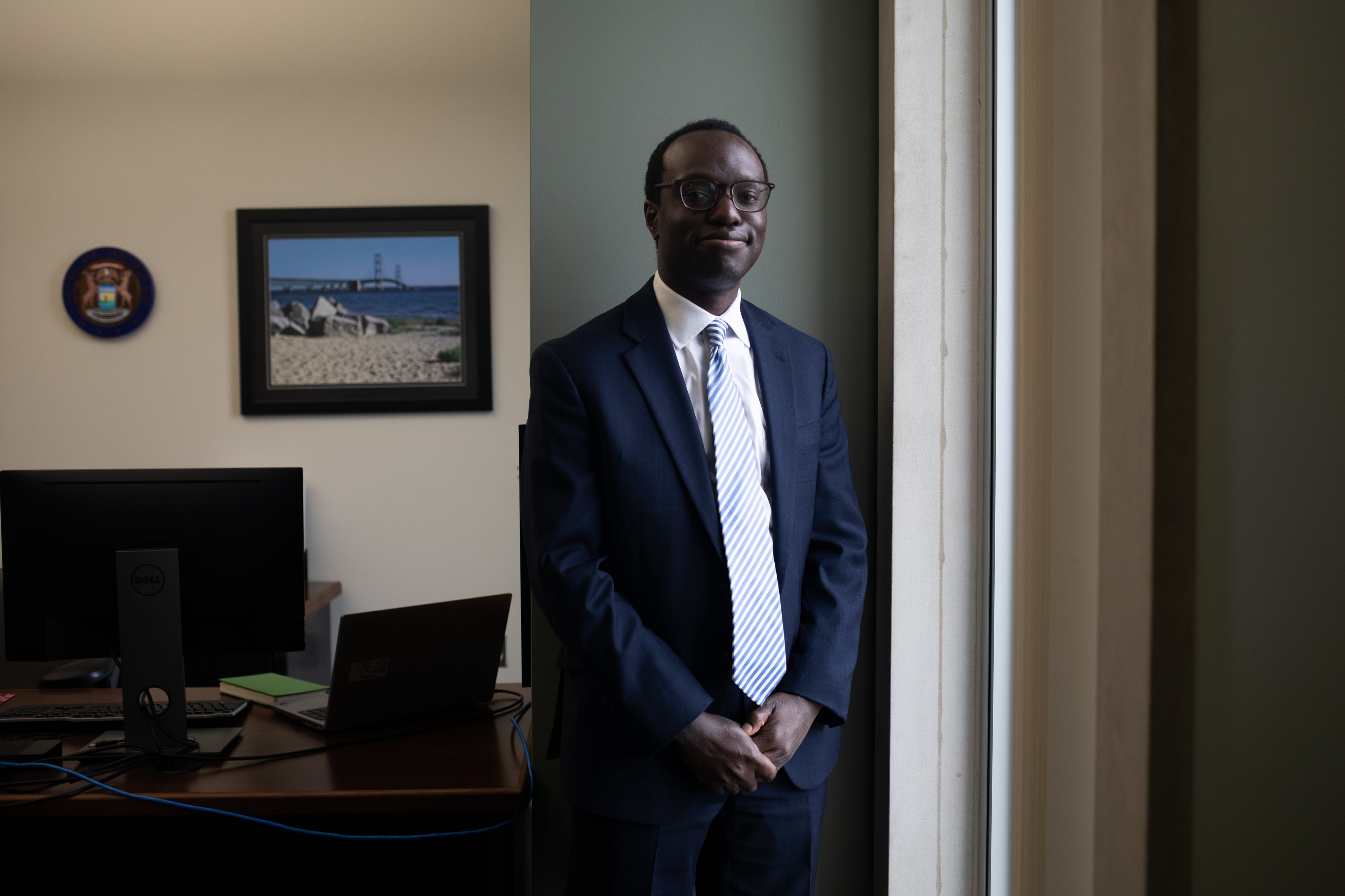 A man in a suit stands next to a window in an office