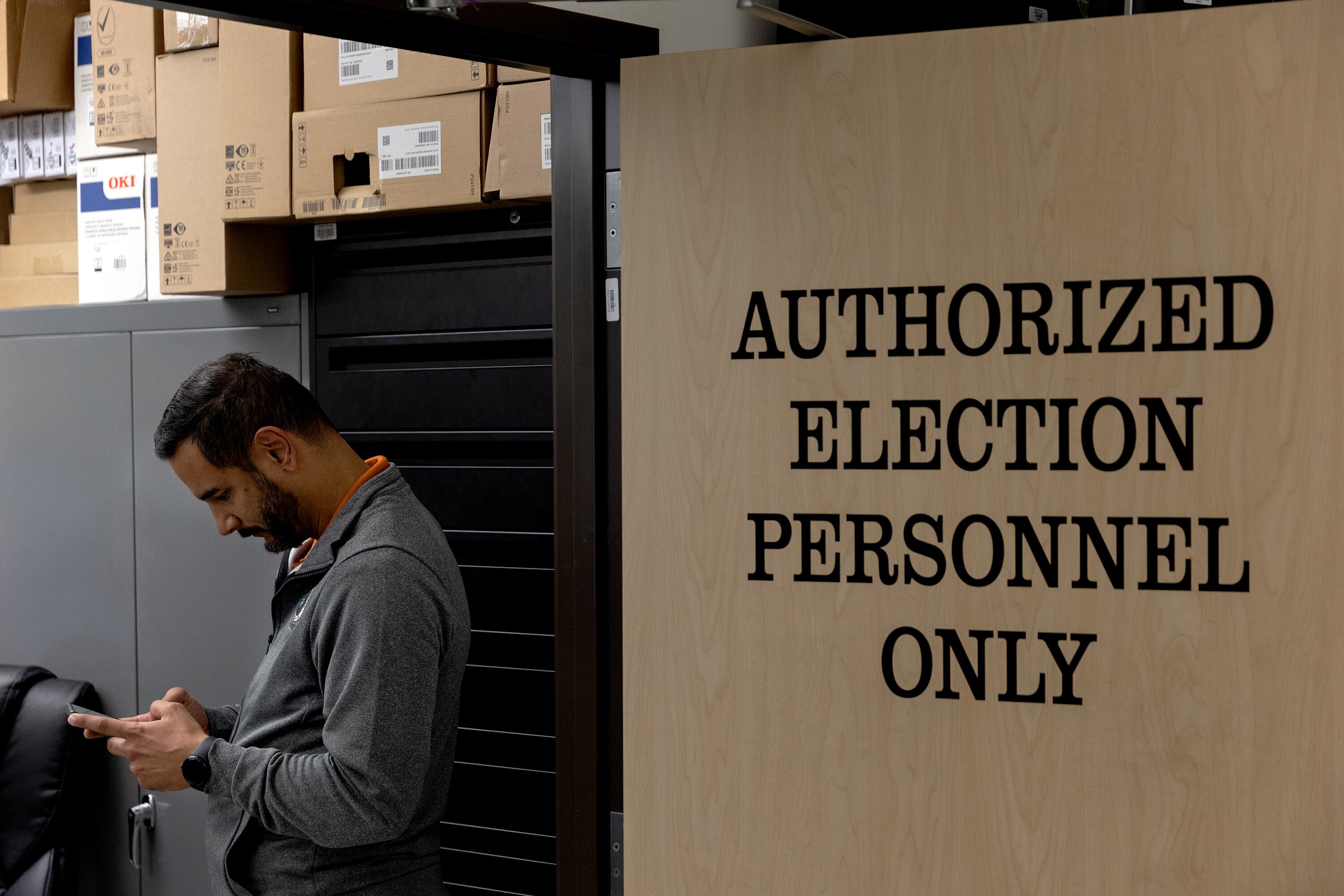 A man stands against a wall, looking down at his phone