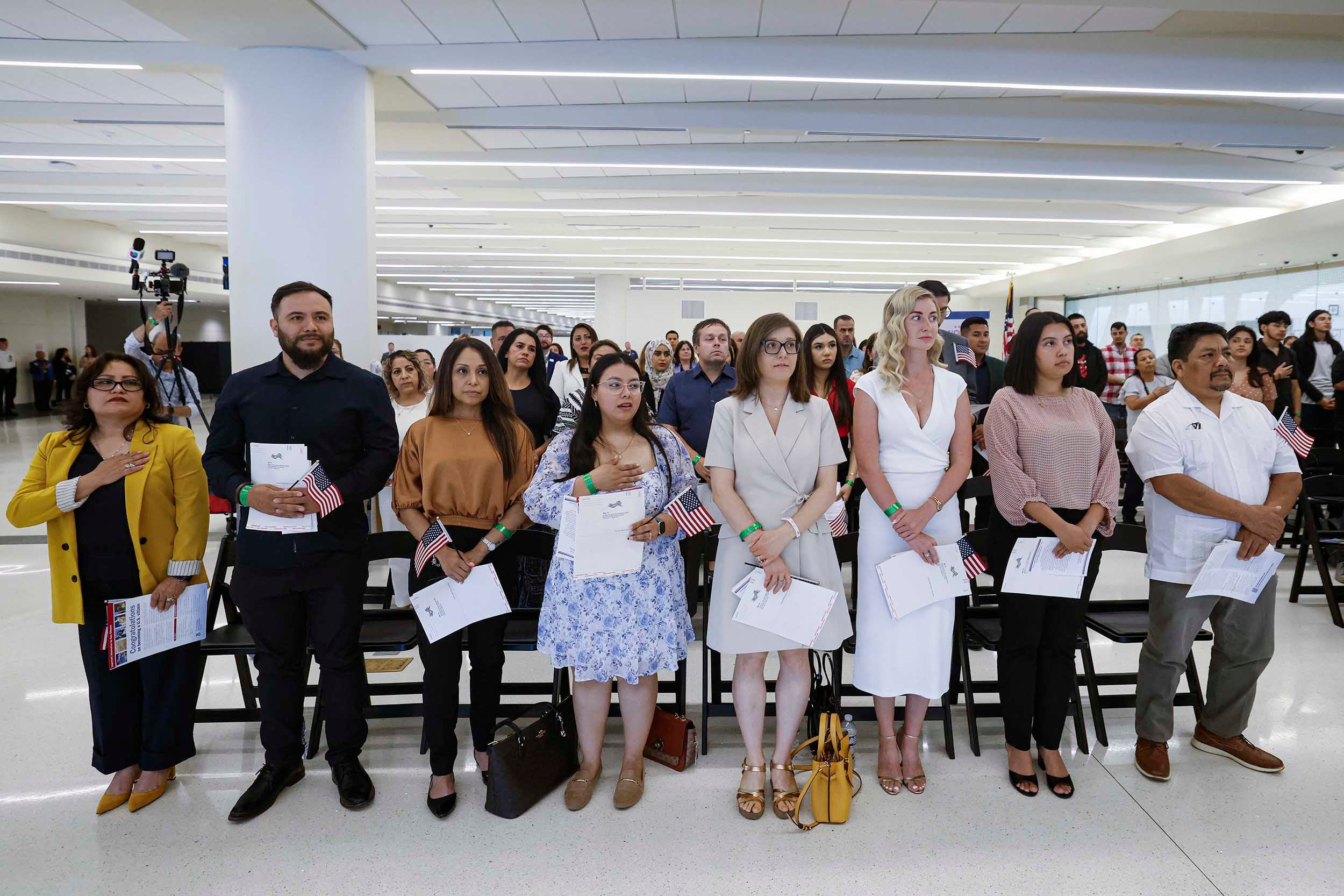 A photograph of a large group of adults standing in rows in a large room taking an oath.