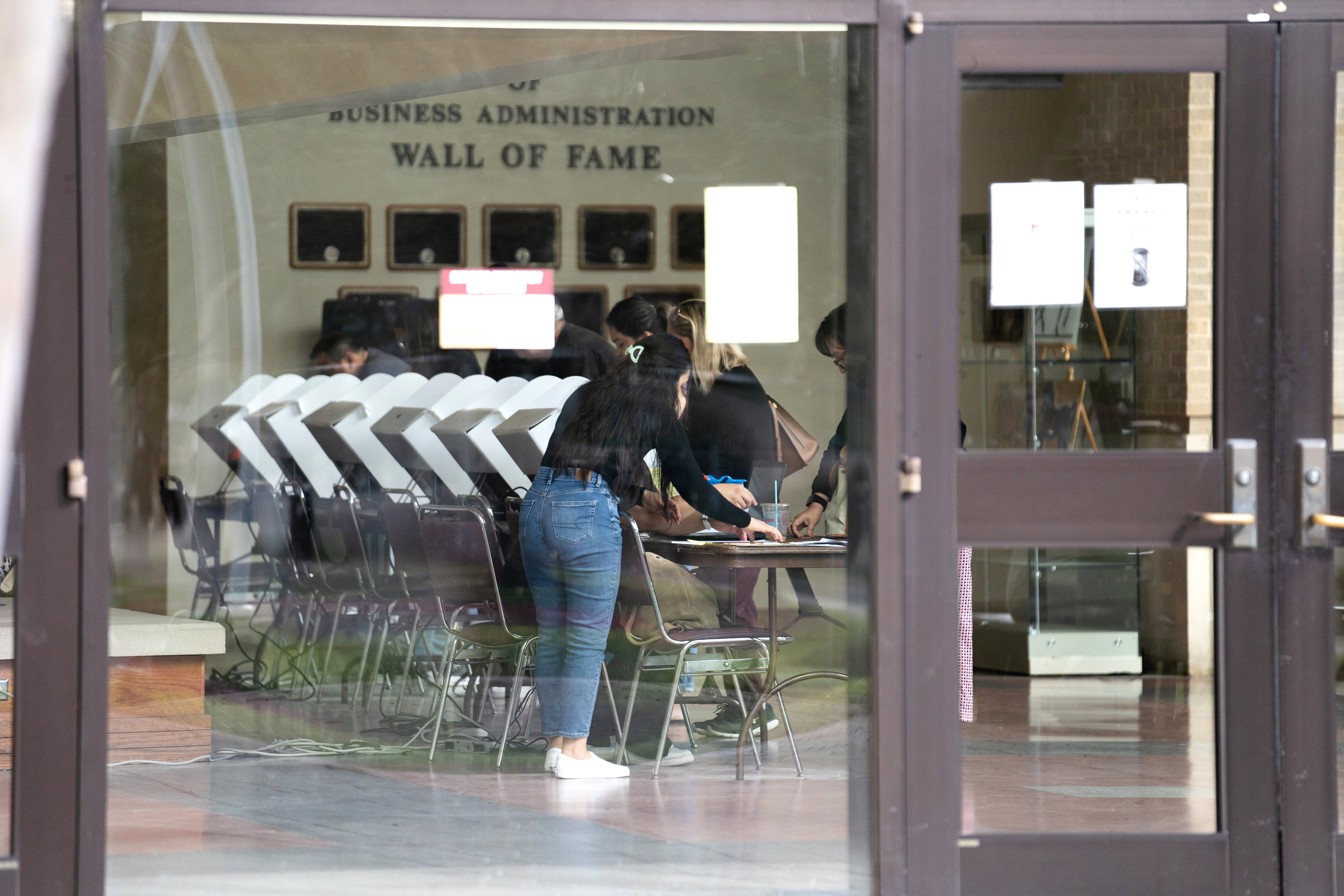 A woman in blue jeans stands before a row of voting booths