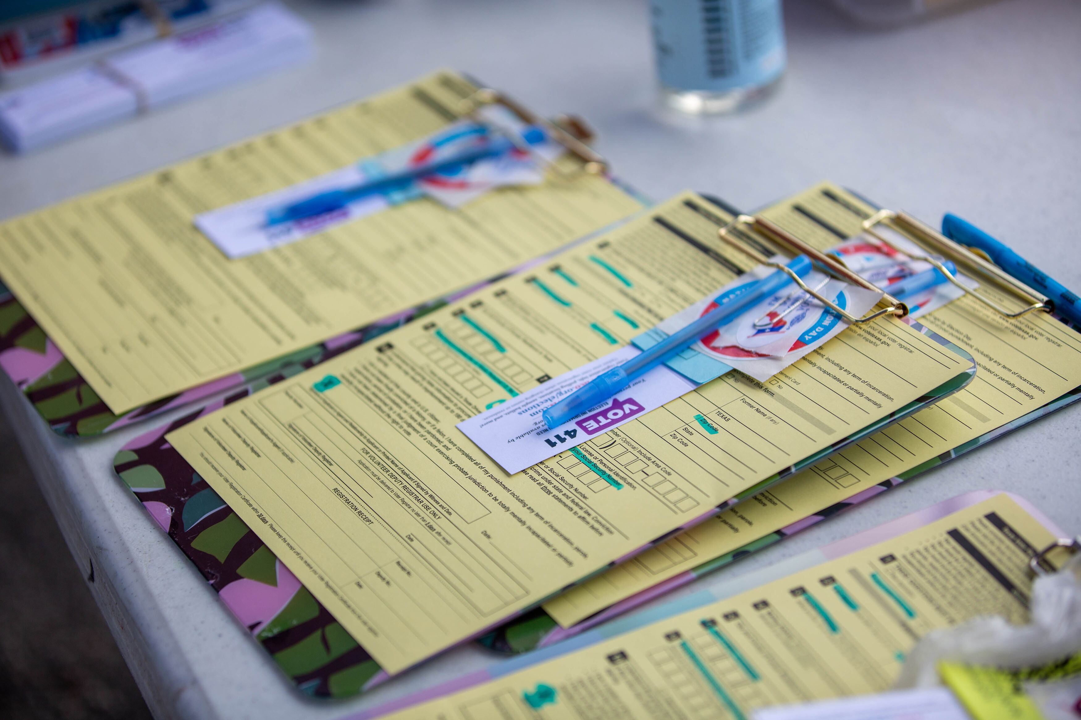 Yellow forms attached to clipboards with blue pens on a white table.