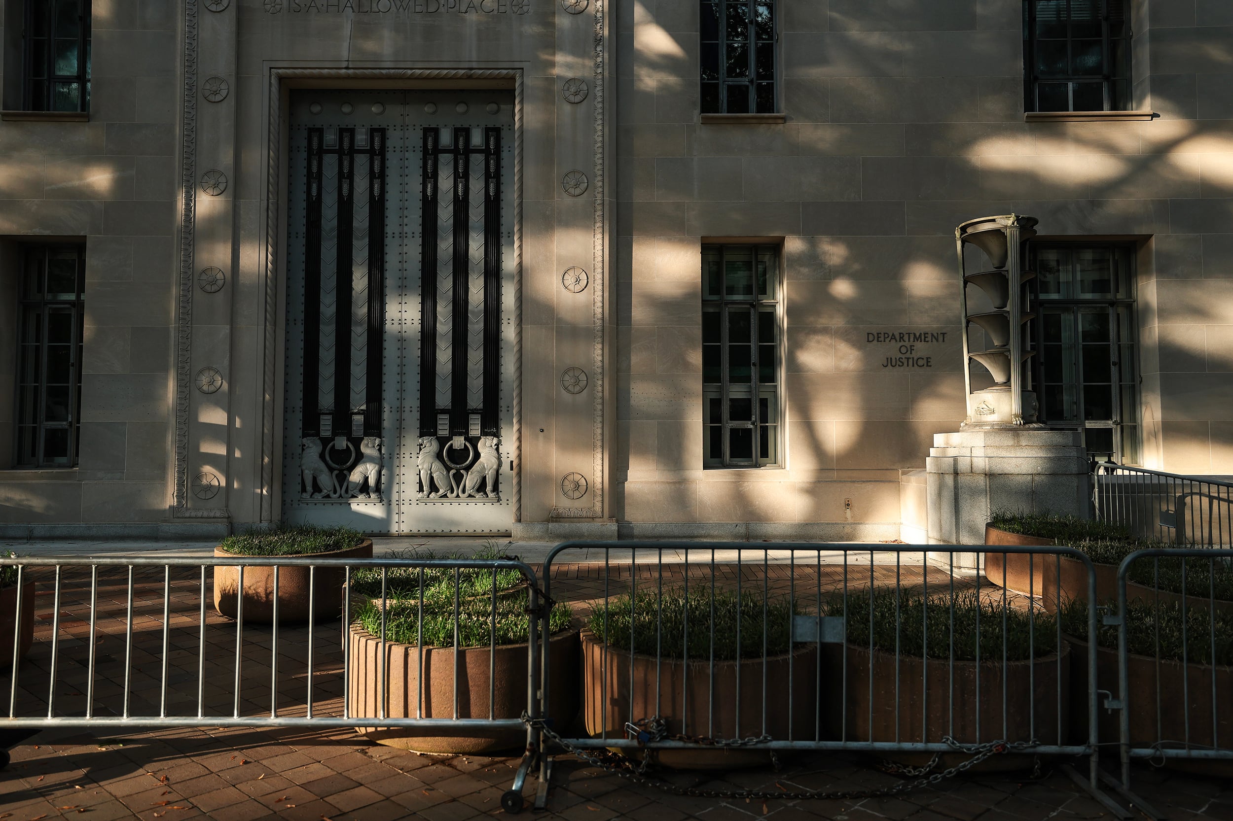 The outside of the U.S. Department of Justice Building on a sunny day with deep shadows on the stone walls from trees.