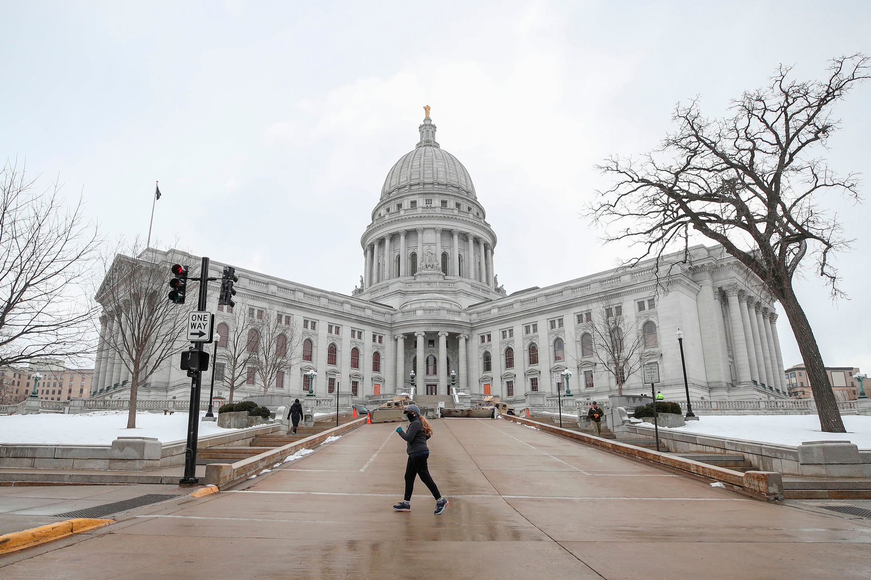 A person walks in front of the Wisconsin State Capitol on a cloudy, cold day.