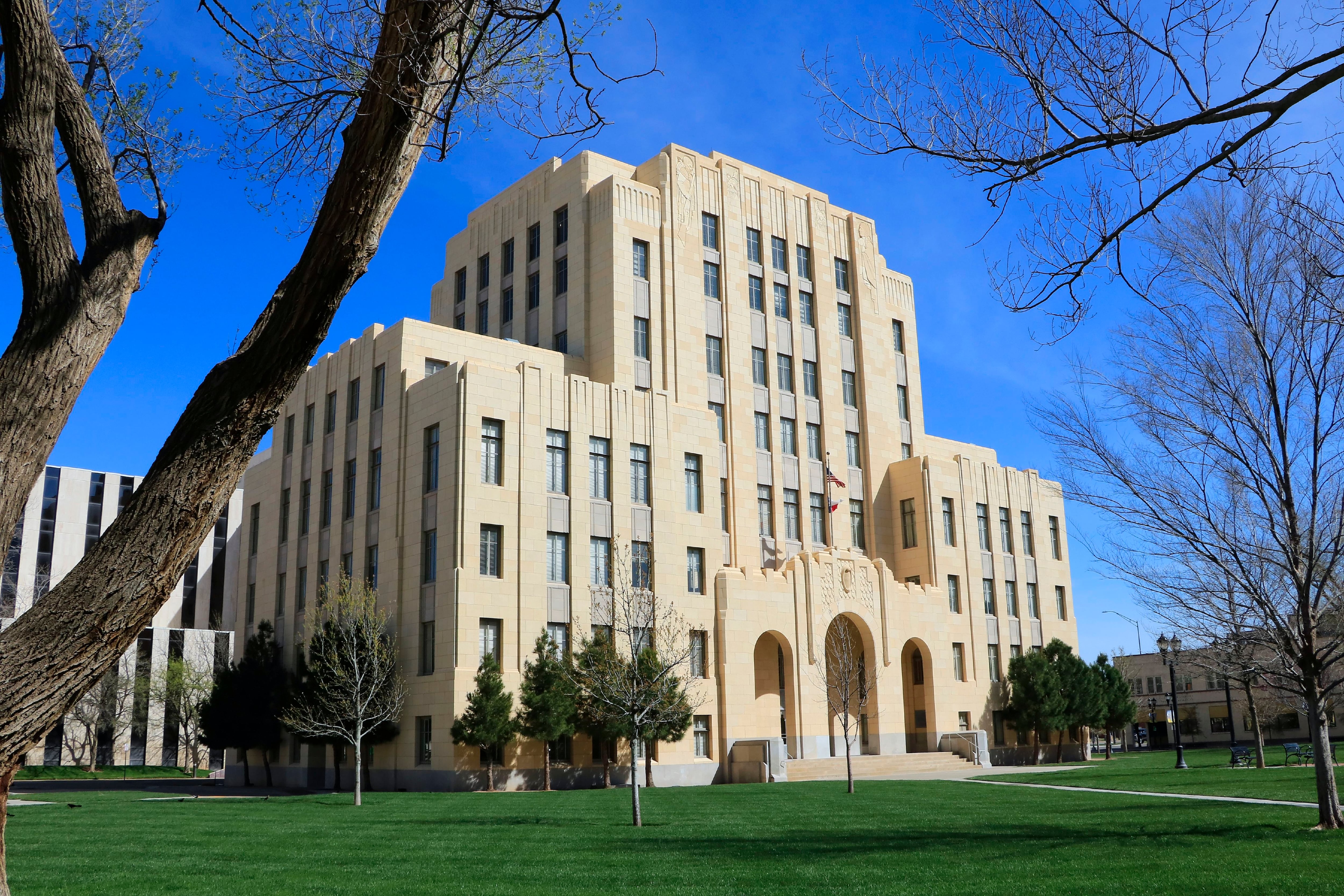 A grand beige building set against a clear blue sky before a lush green lawn, tree limbs visible on edges of frame