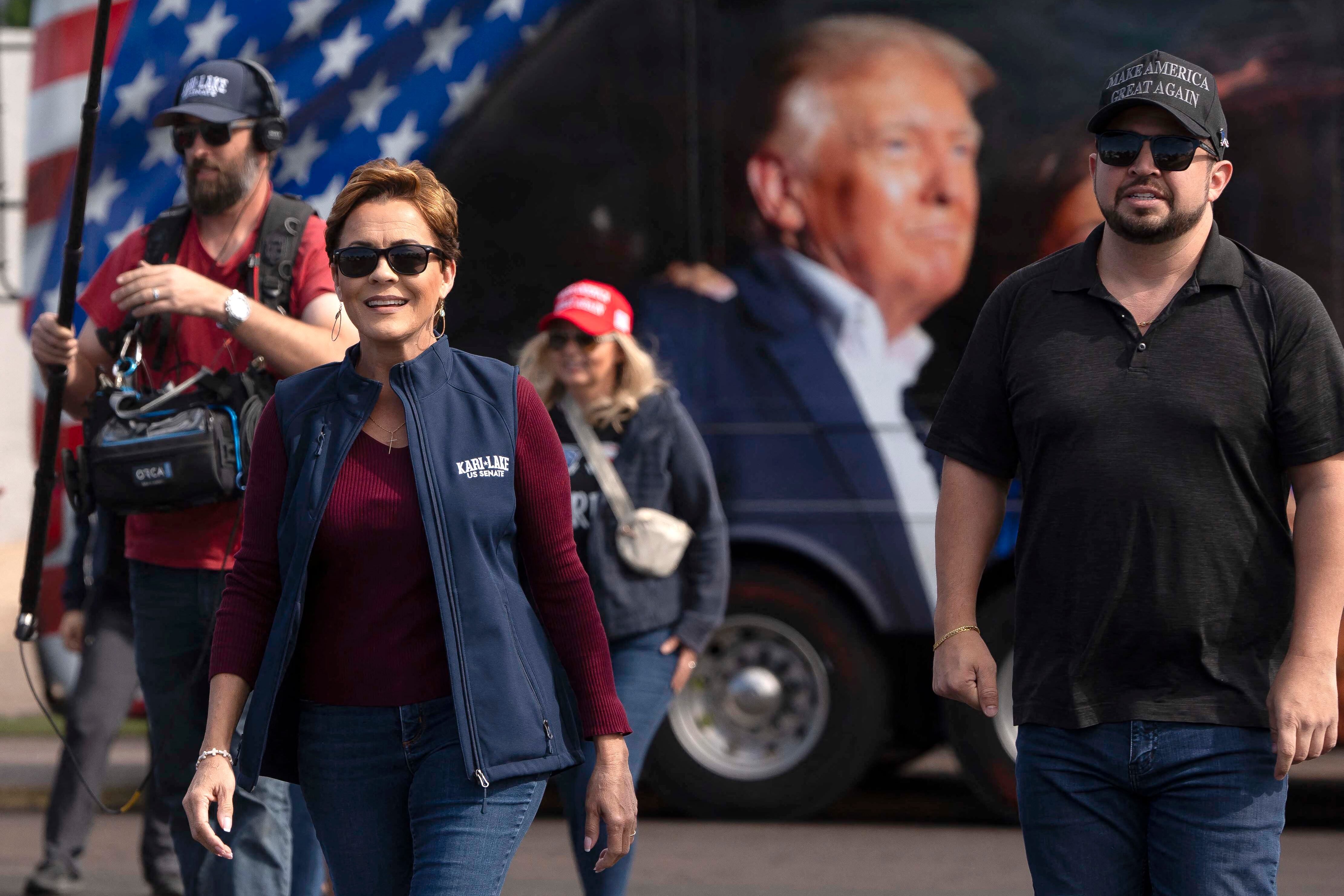Four people walk in front of a large bus that has a photo of Trump on the side.