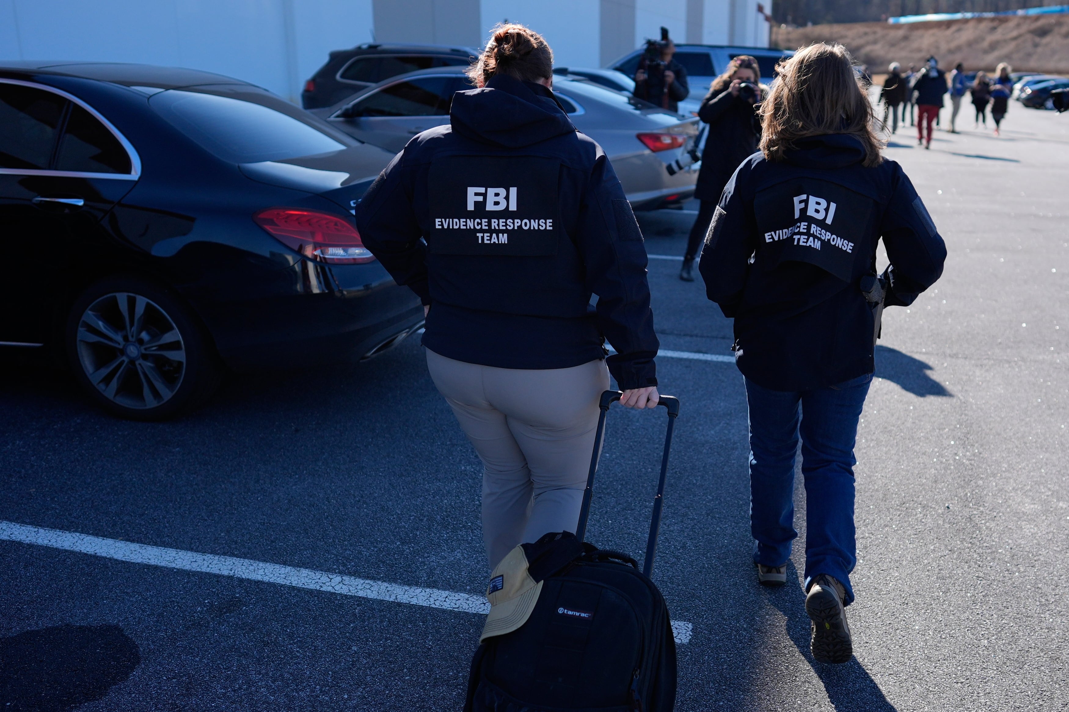 A photograph of two people wearing black sweaters with the words "FBI" on it walking next to a large building with some people far off in the distance.