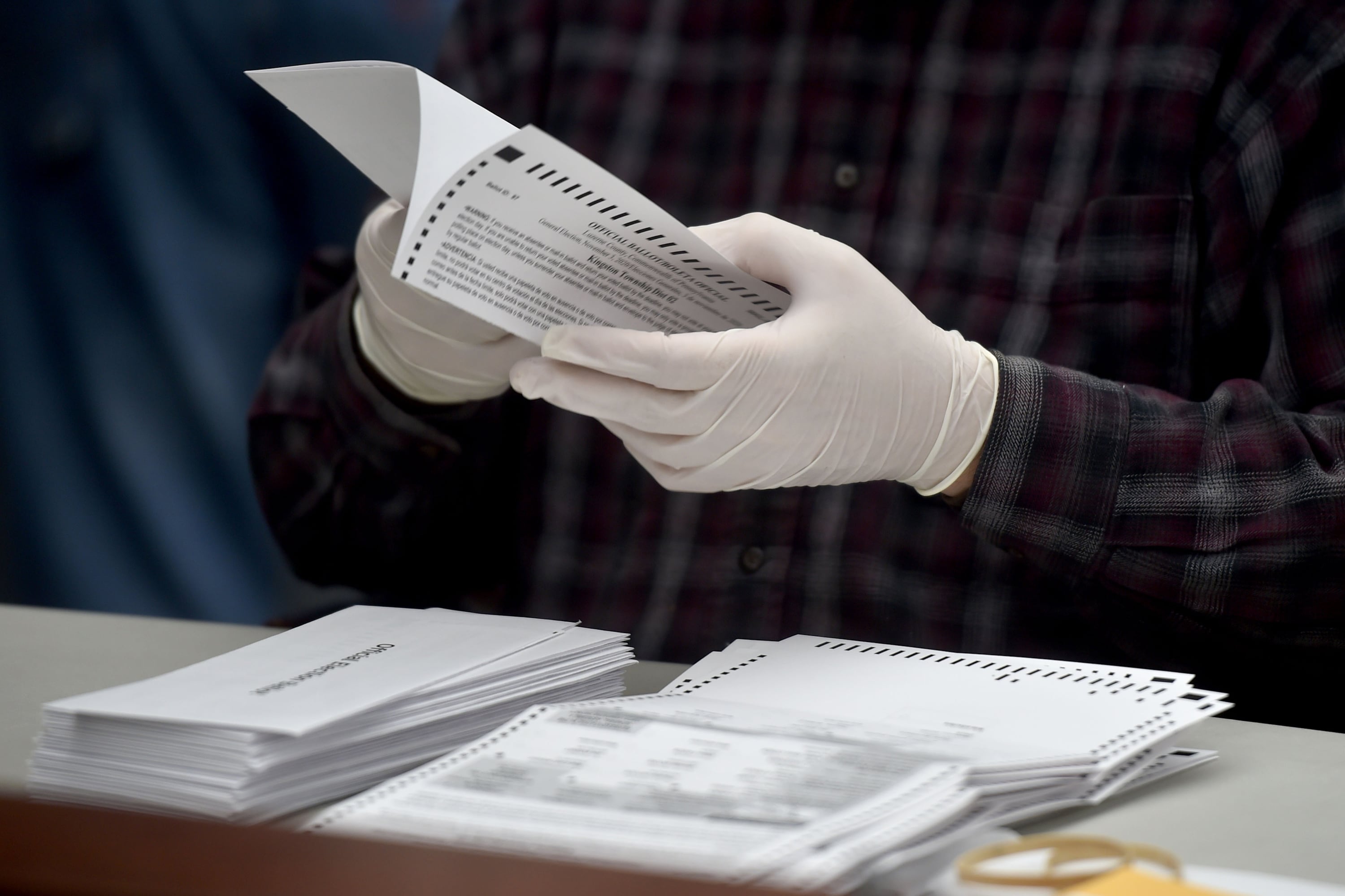 County employee's hands open mail-in ballots while wearing gloves.