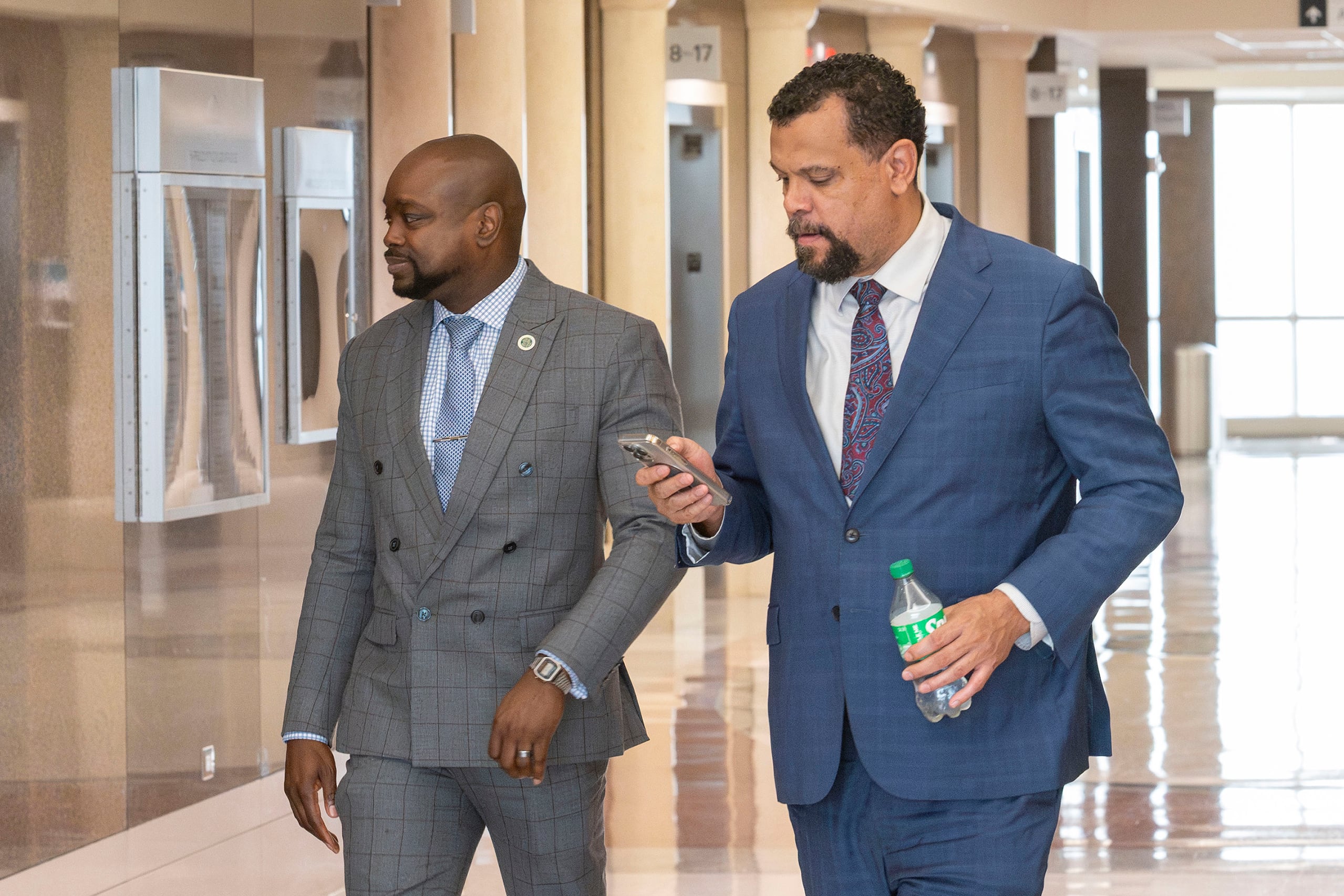 Two men in suits walk down a hallway together.