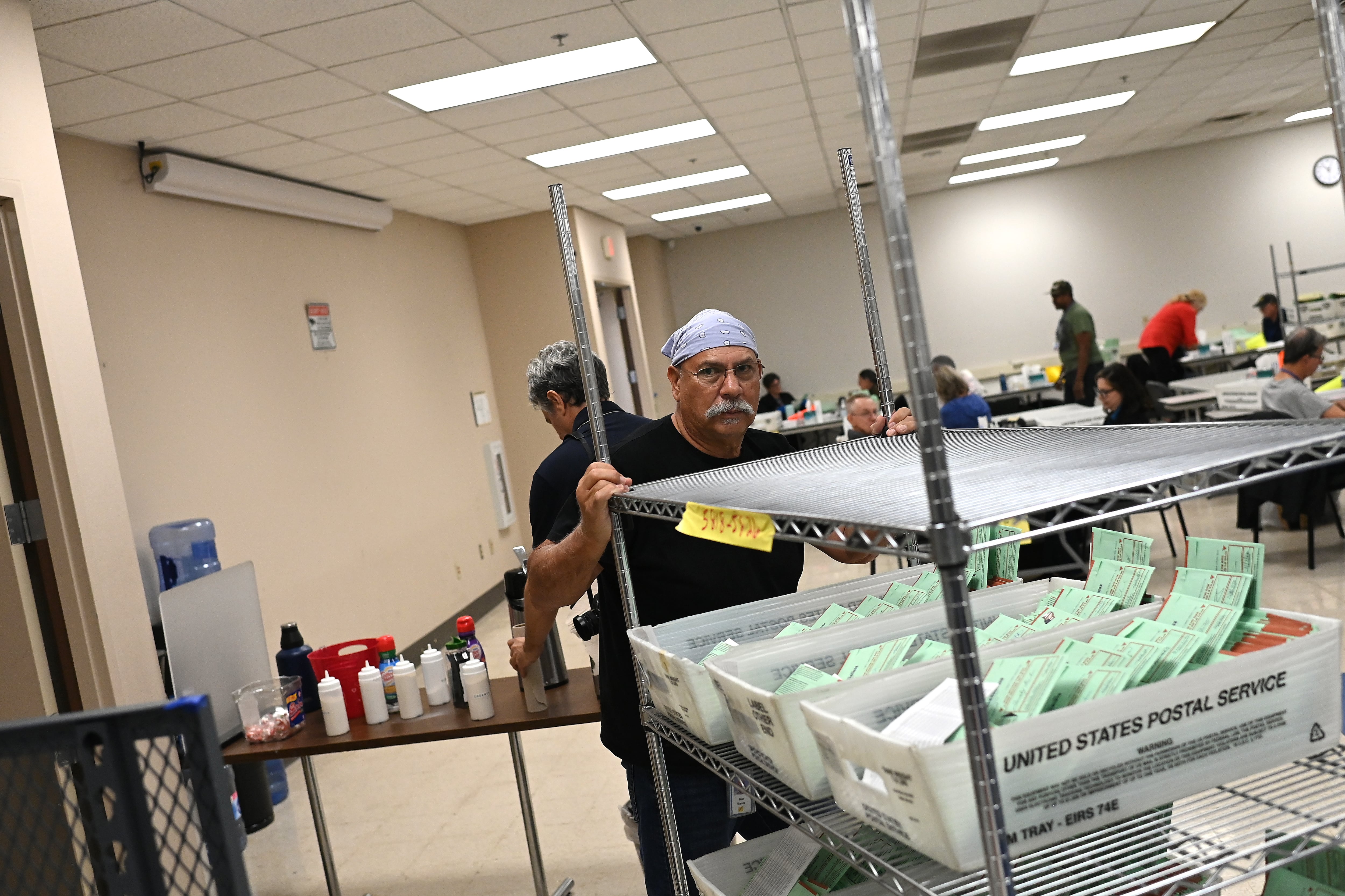 Man pushes cart of green ballot envelopes in warehouse