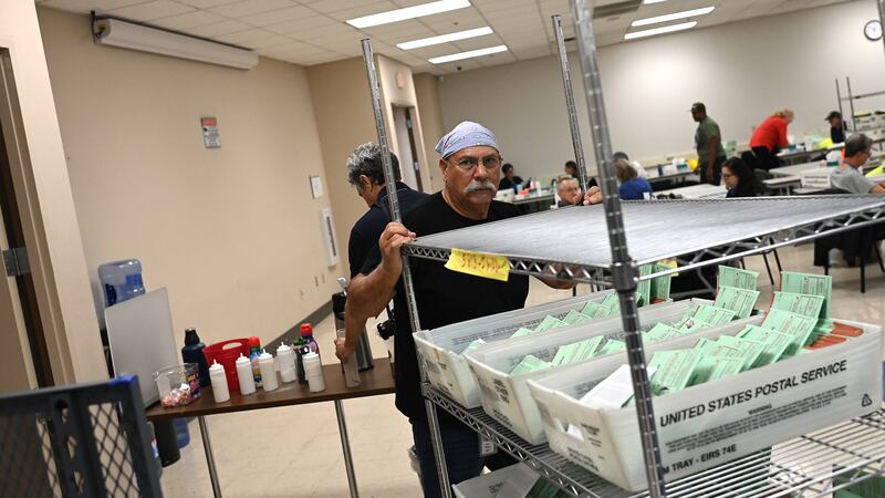 Man pushes cart of green ballot envelopes in warehouse