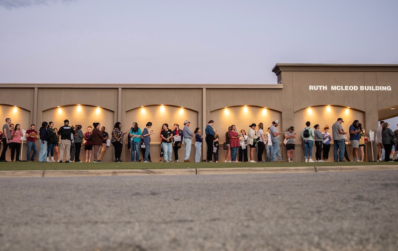 A long line of voters stand outside of a building.