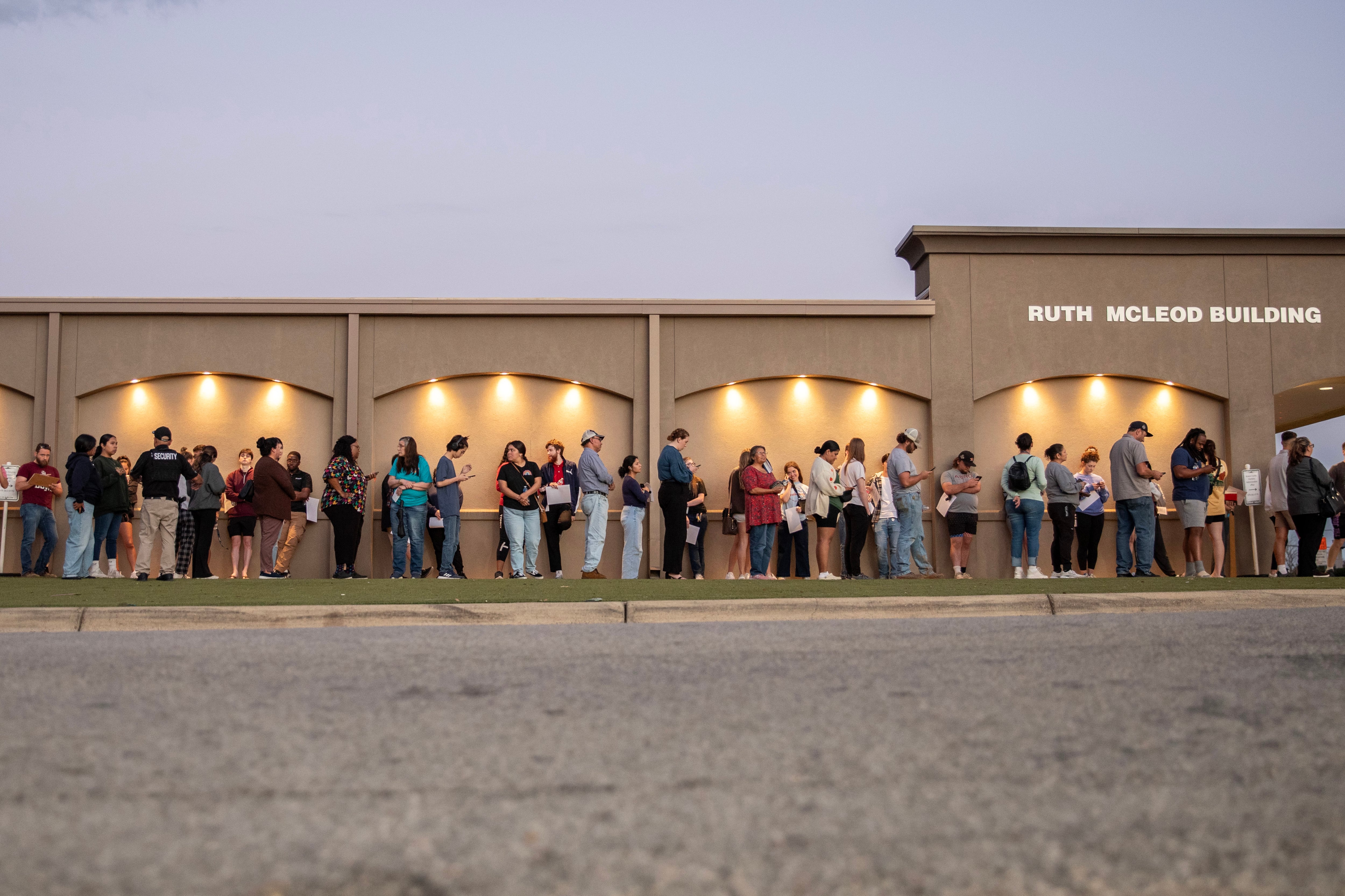 A long line of voters stand outside of a building.