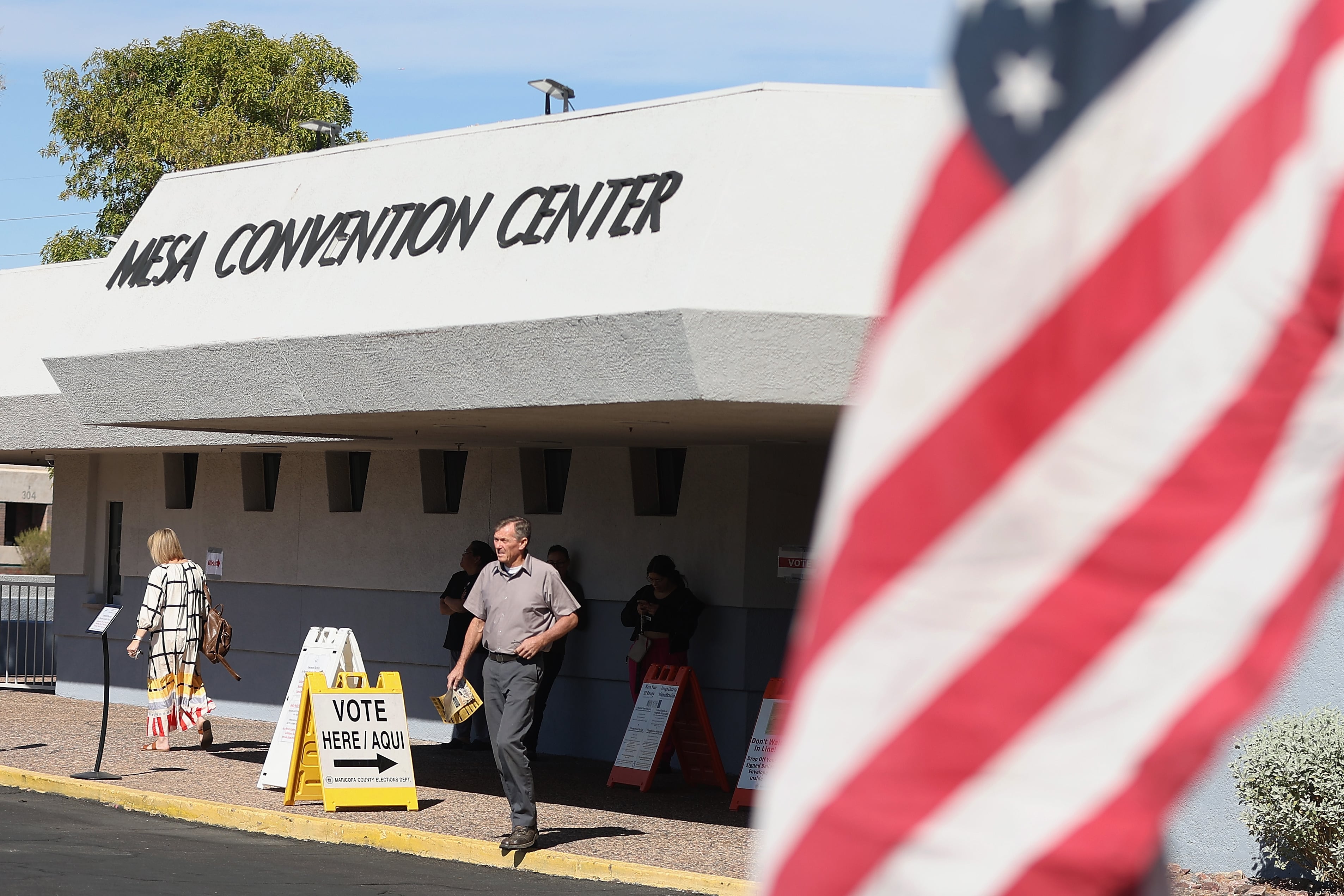 A man walks out of a building with a flag flying in the foreground.