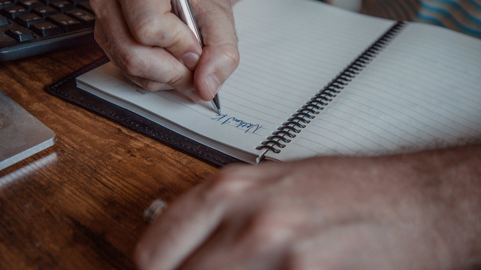 A close up of a hand holding a pen writing in a notebook.