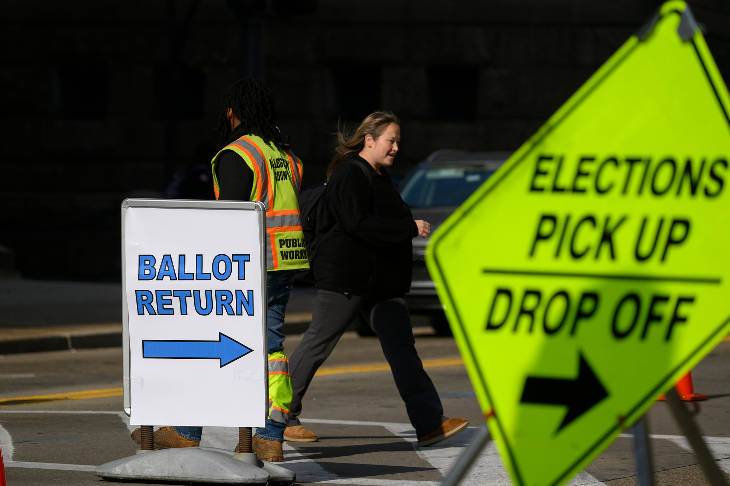 A person walks behind two signs that are sandwiching her outside on a crosswalk.