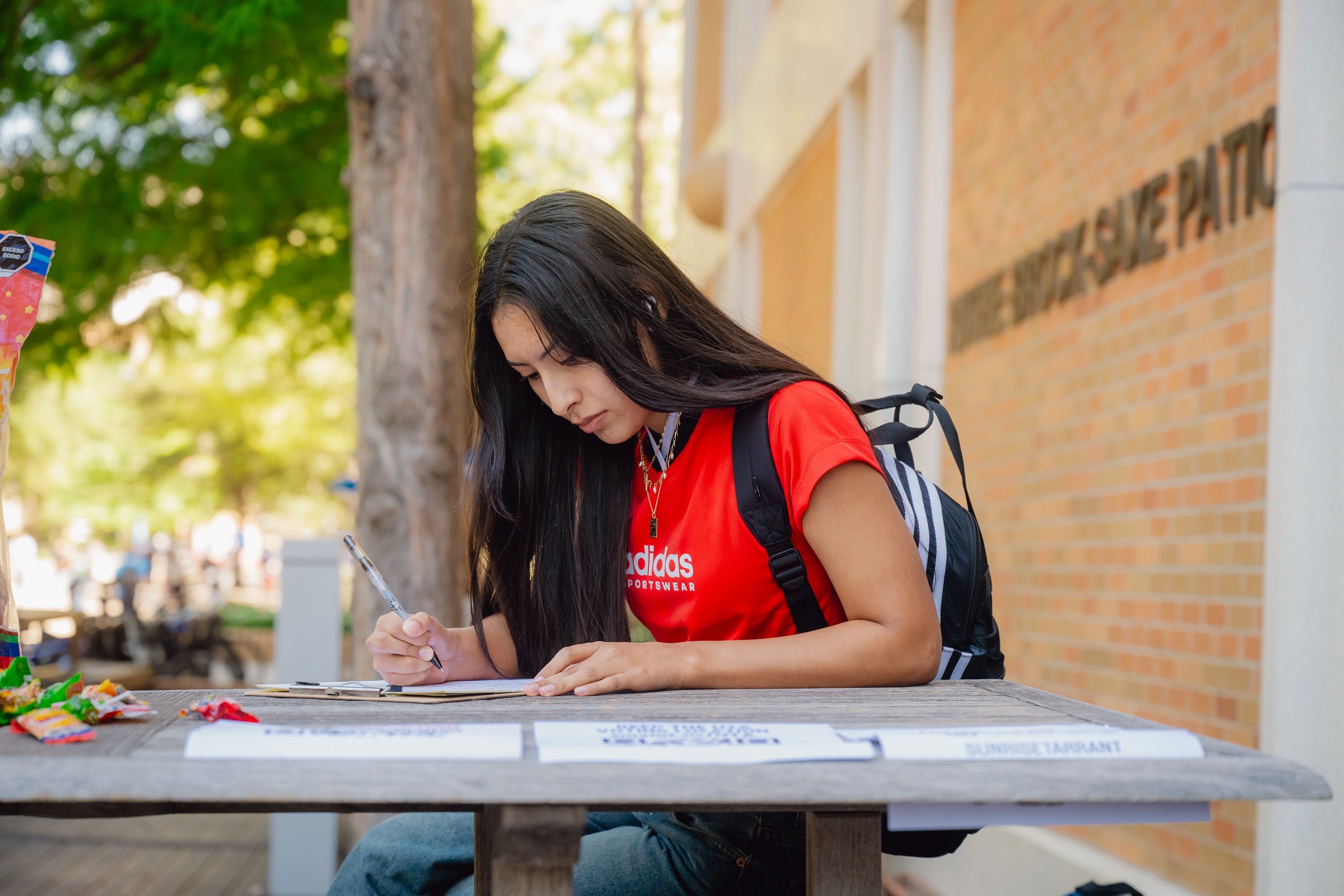 A woman with dark hair and a red short fills out paperwork at a table.