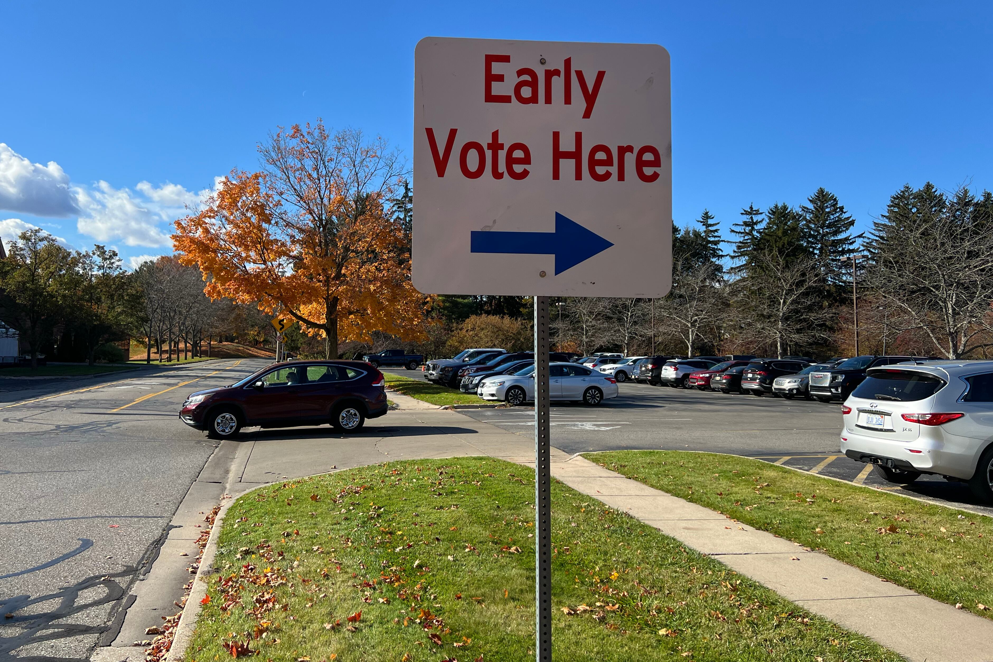A car leaves a full parking lot and behind a sign that reads "Early Vote Here."