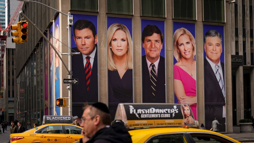 The side of a building on a busy street featuring large portrait photos of familiar TV newspeople.