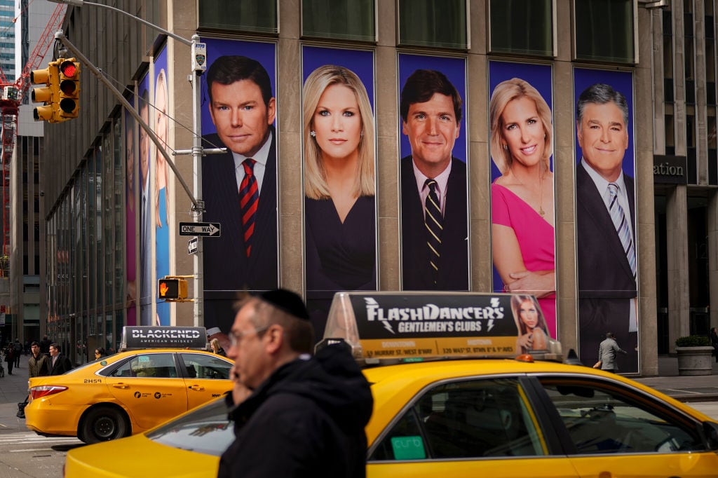The side of a building on a busy street featuring large portrait photos of familiar TV newspeople.