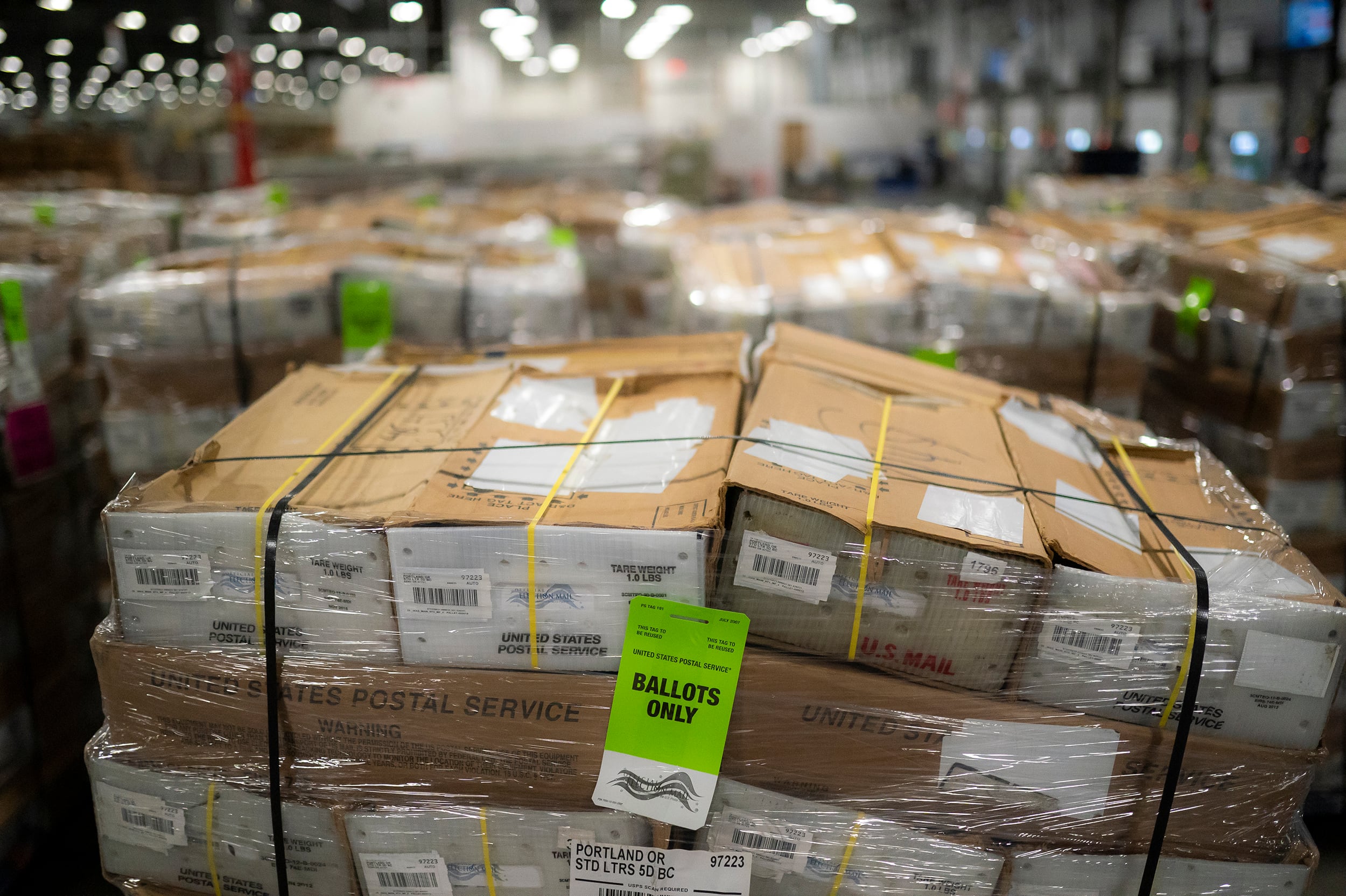 A photograph of boxes full of mail in ballots wrapped in plastic wrap in a large warehouse.