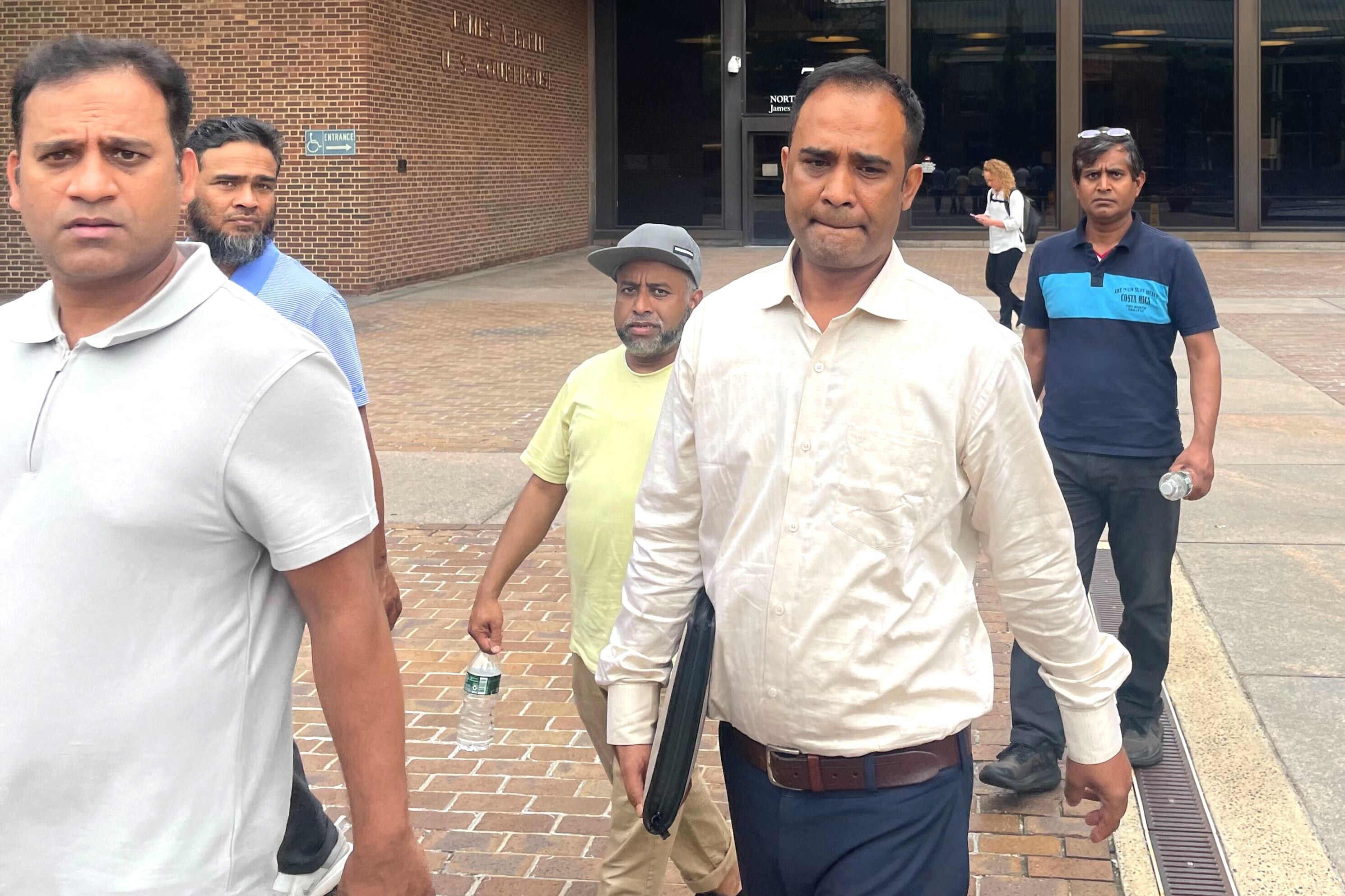 A man in a light shirt walks surrounded by other people.