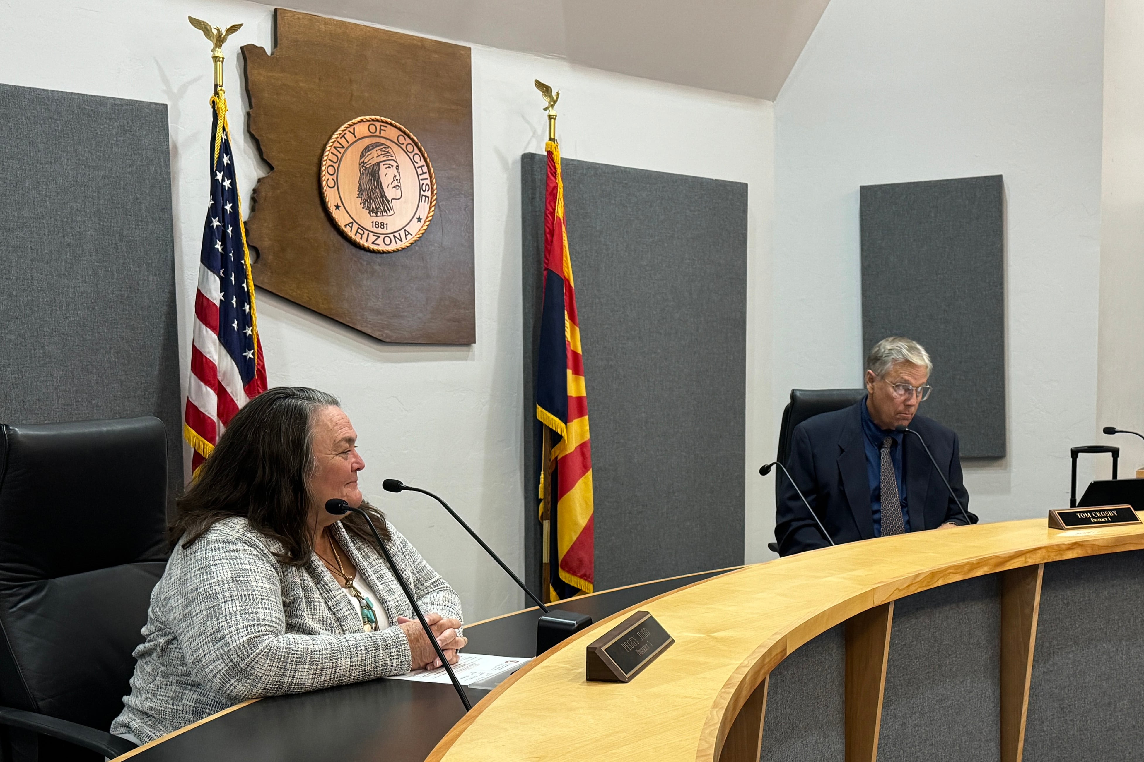 Two people sit behind a large wooden table and microphones in a courtroom.