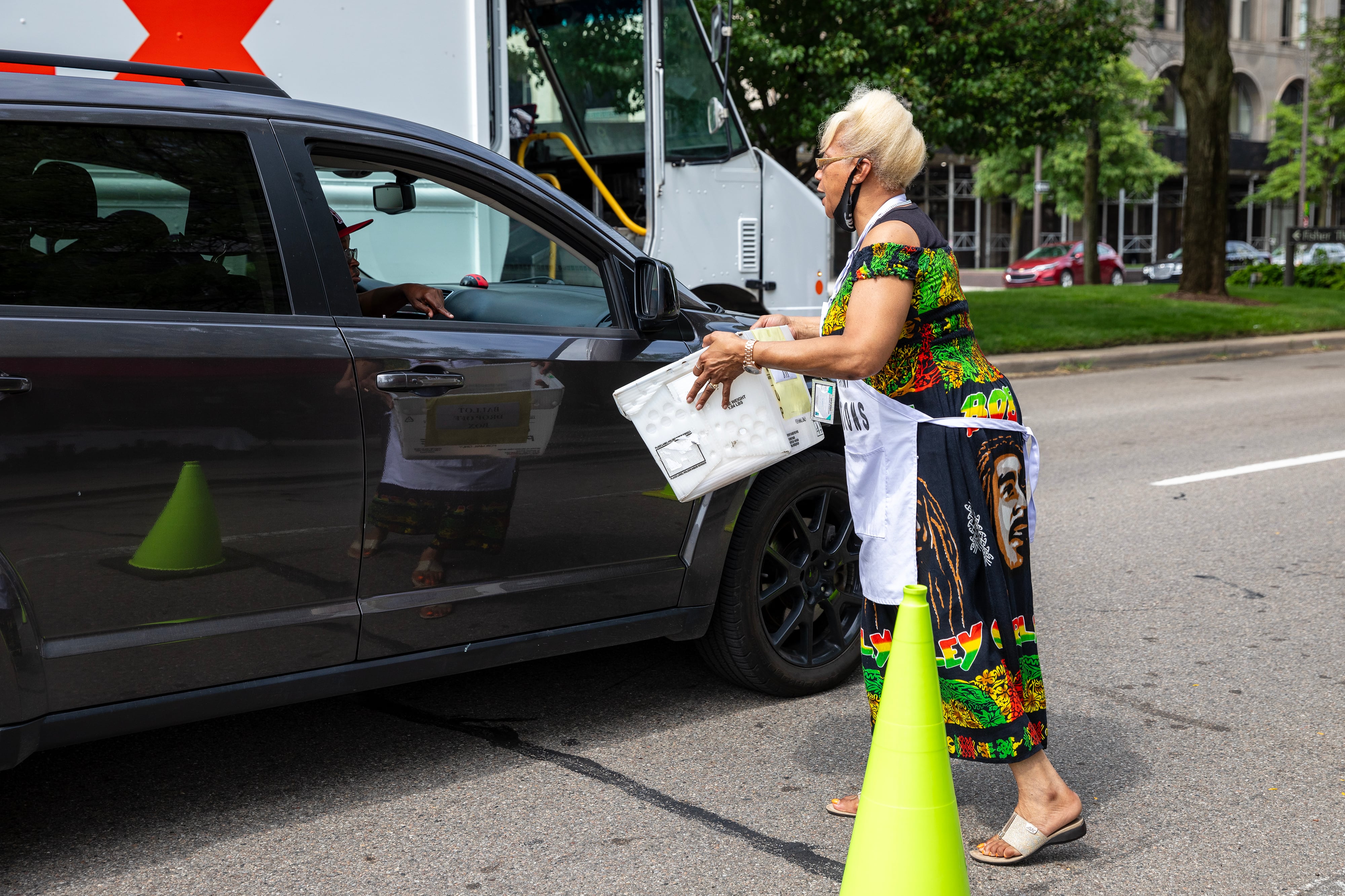 A woman stands outside of a car next to a yellow safety cone.