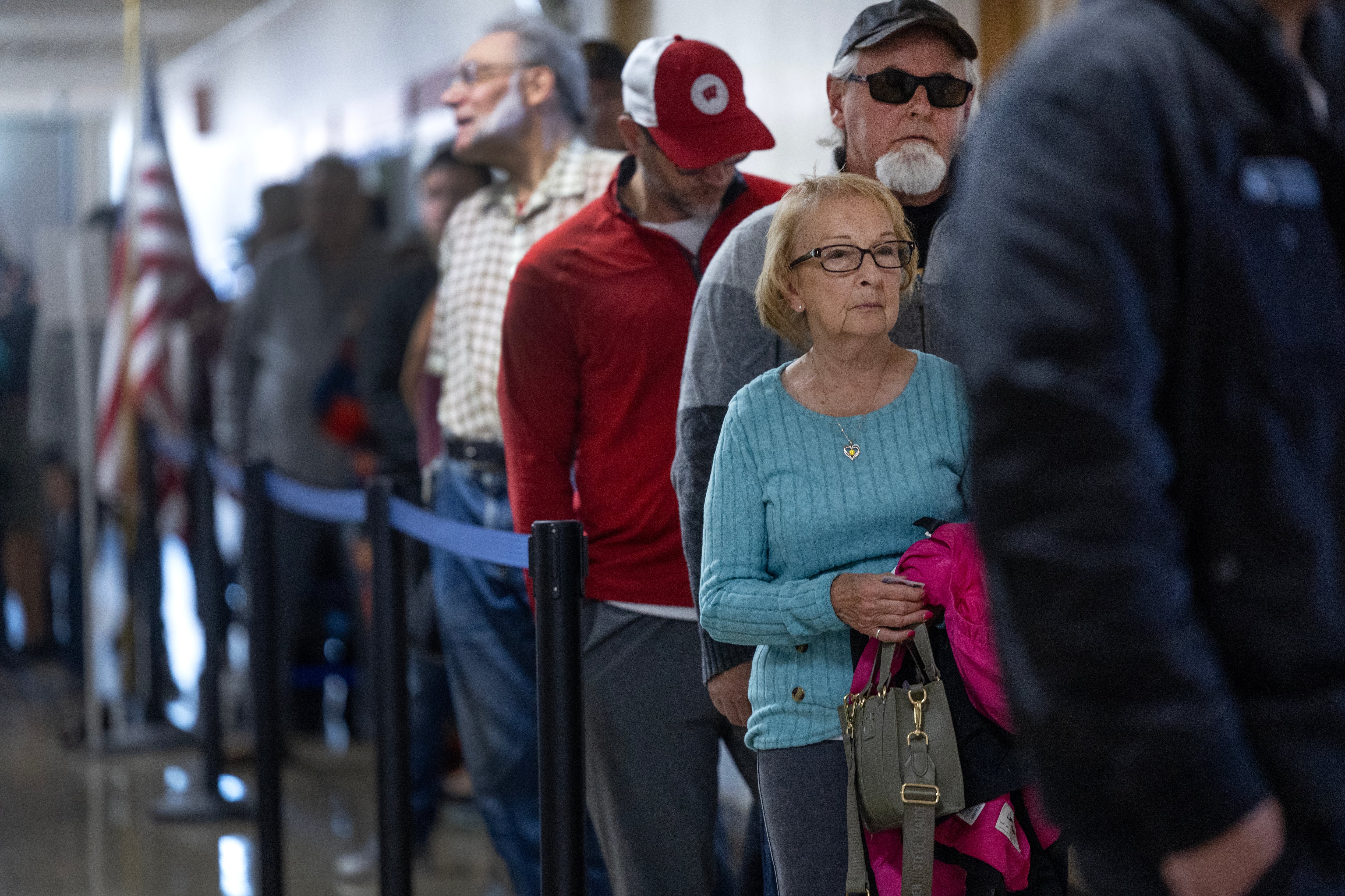 A woman with a blue top and glasses is standing in a long line of people