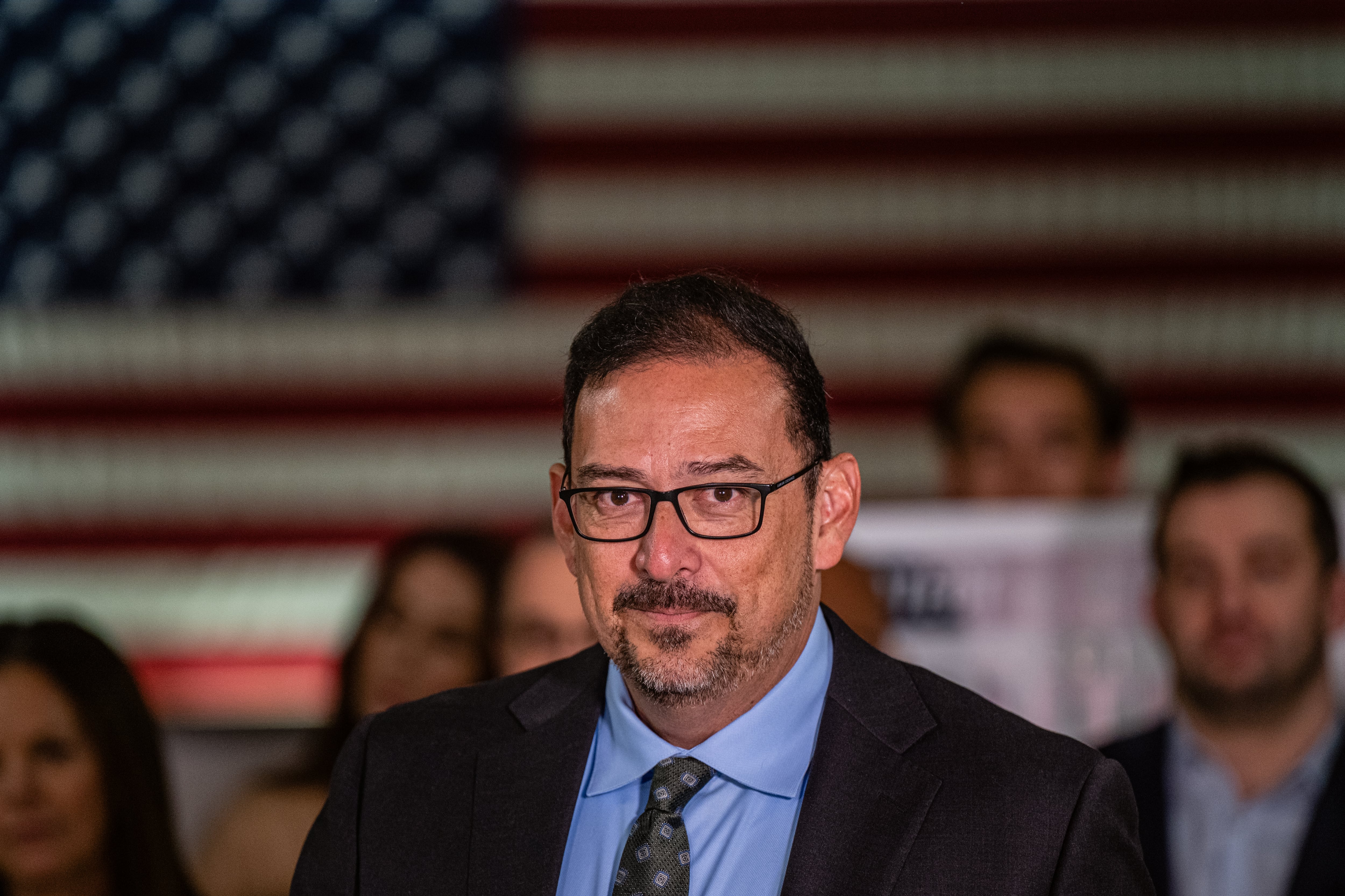 man in suit looks at camera with american flag background